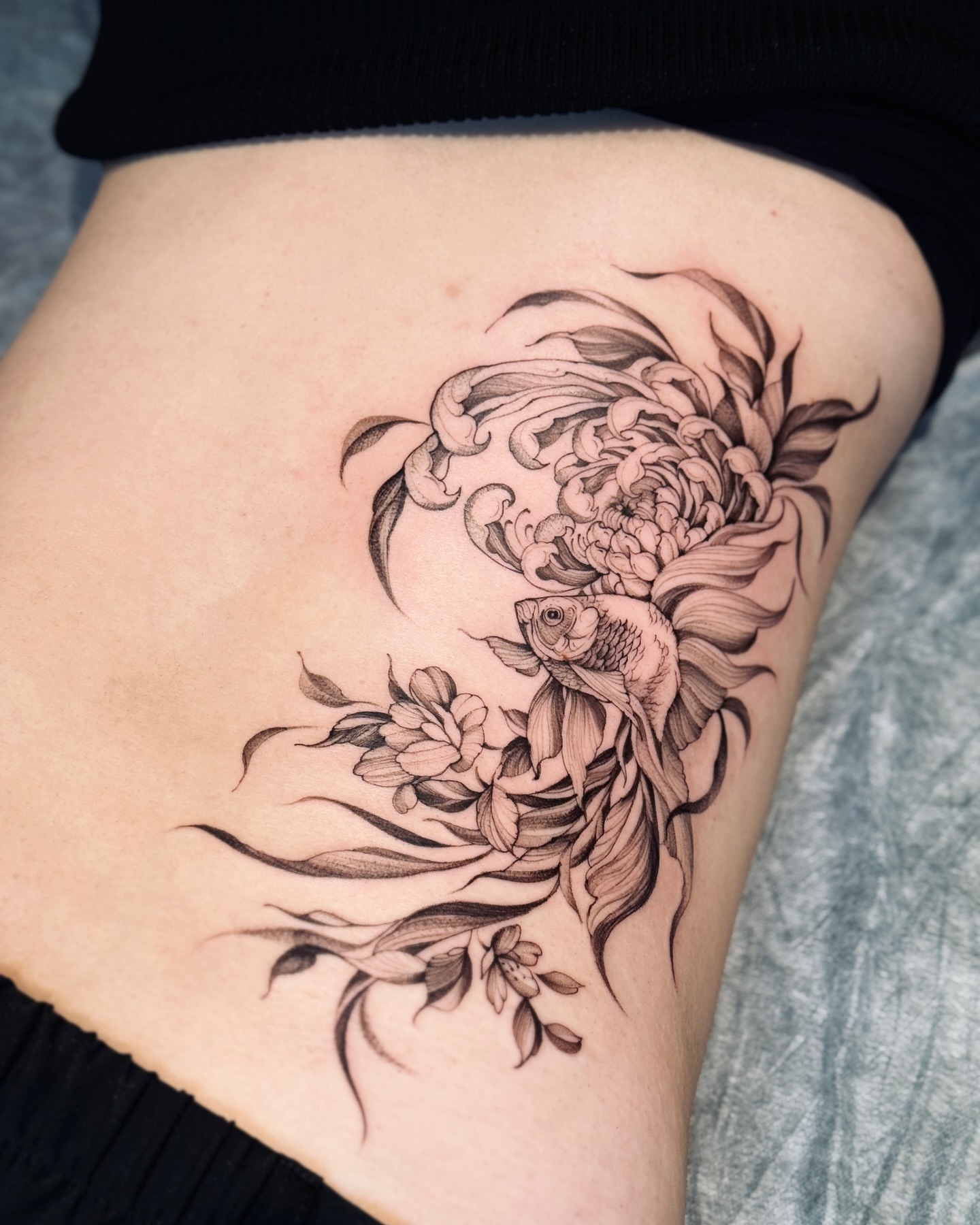 Goldfish and flowers realism tattoo on the thigh by Dung Ngo