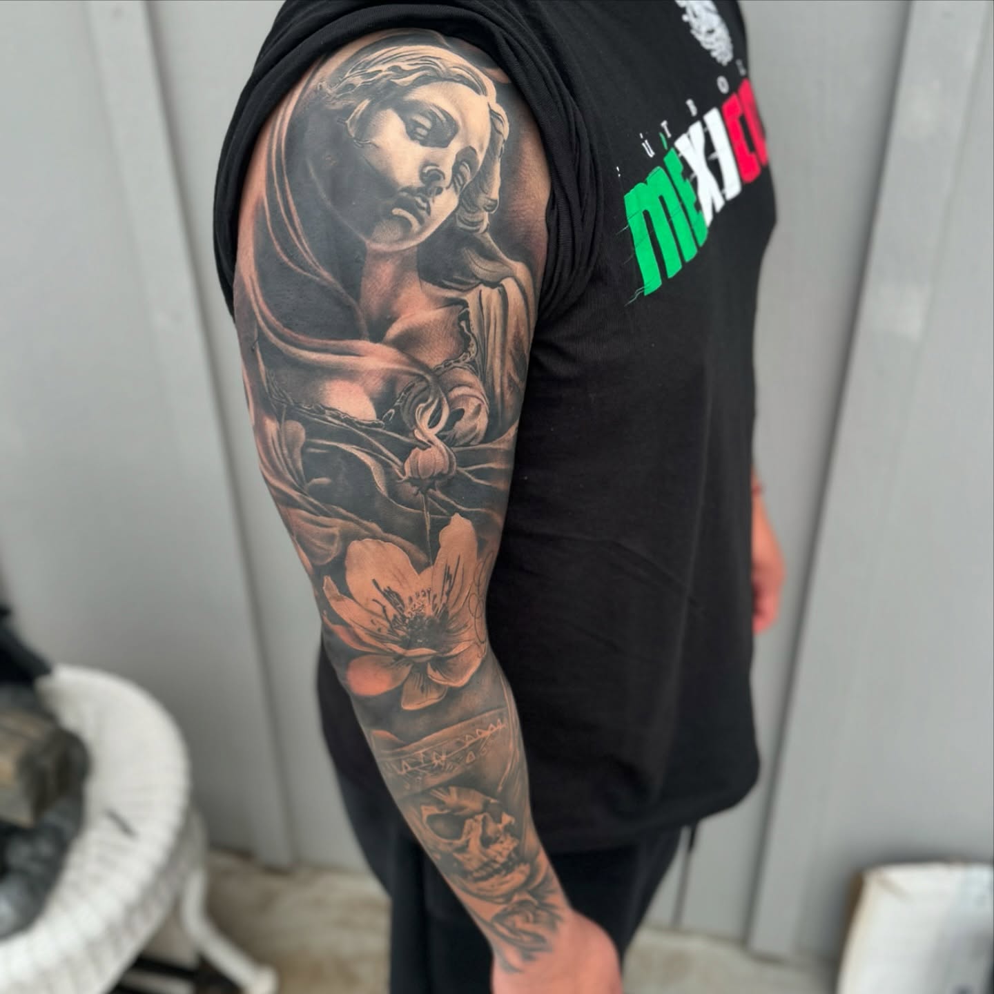 Religious figure with flower realism tattoo on the upper arm by Angel Pineda-Rodriguez