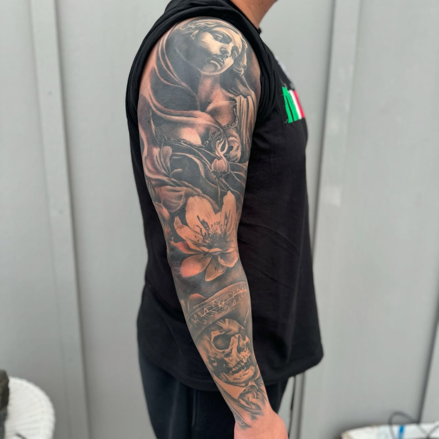 Woman with flowers and skull realism tattoo on the upper arm by Angel Pineda-Rodriguez