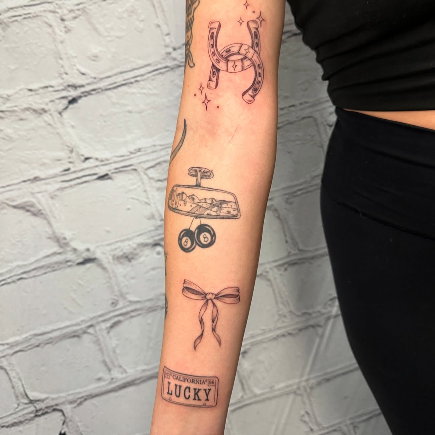 Horseshoe, pool balls, bow, license plate black and grey tattoo on the forearm by Stephen Hansen