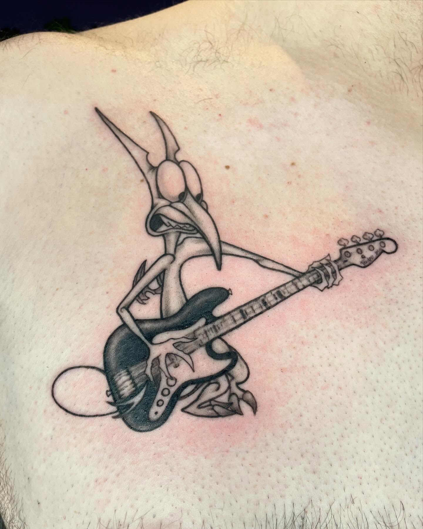 Roadrunner playing guitar black and grey tattoo on the back by Christin Baumgart