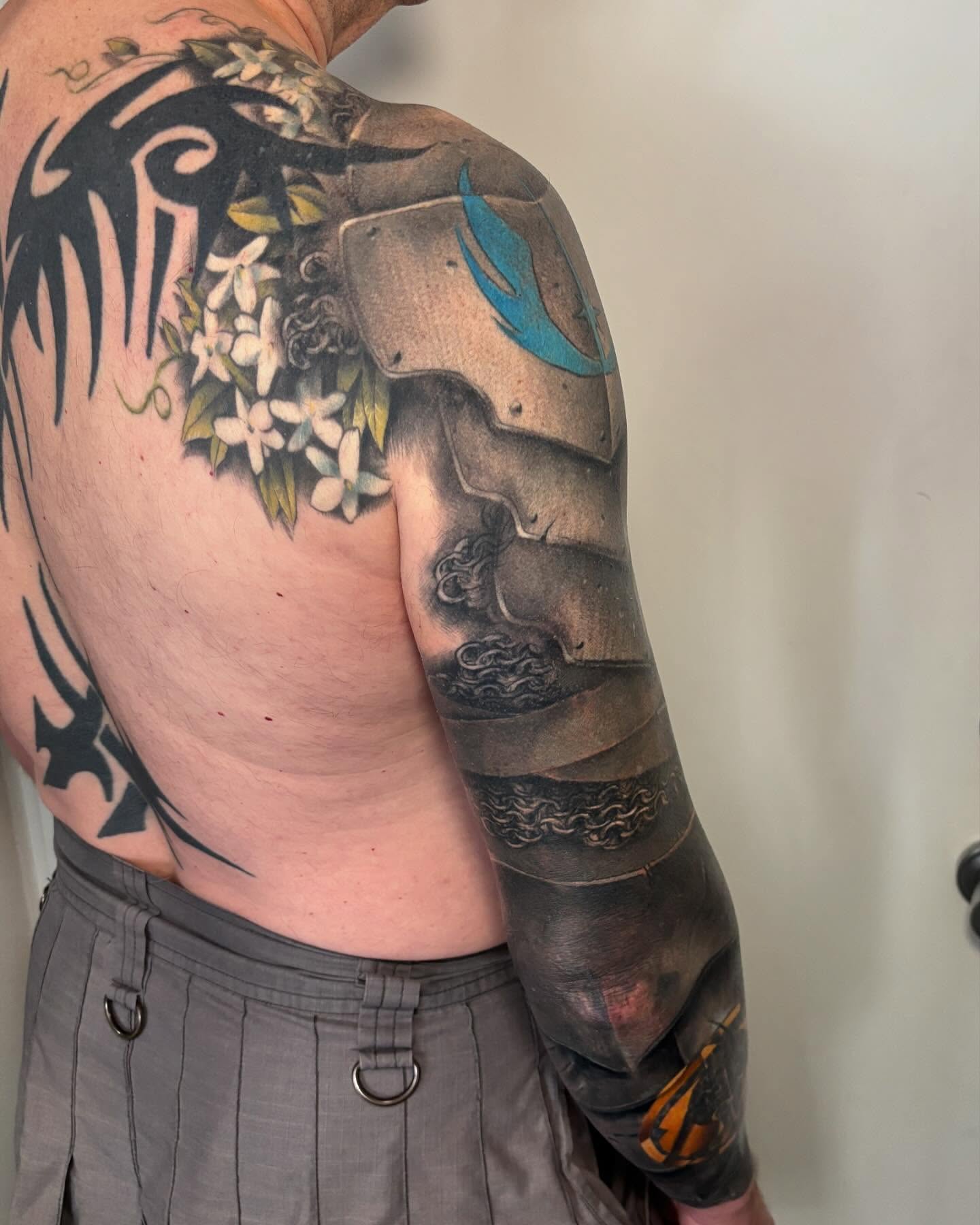 Warrior armor and flowers realism tattoo on the upper arm by Ericksen Linn