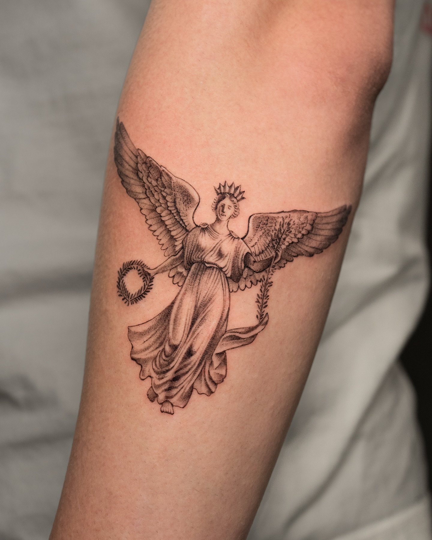 Winged figure black and grey tattoo on the forearm by Mateo