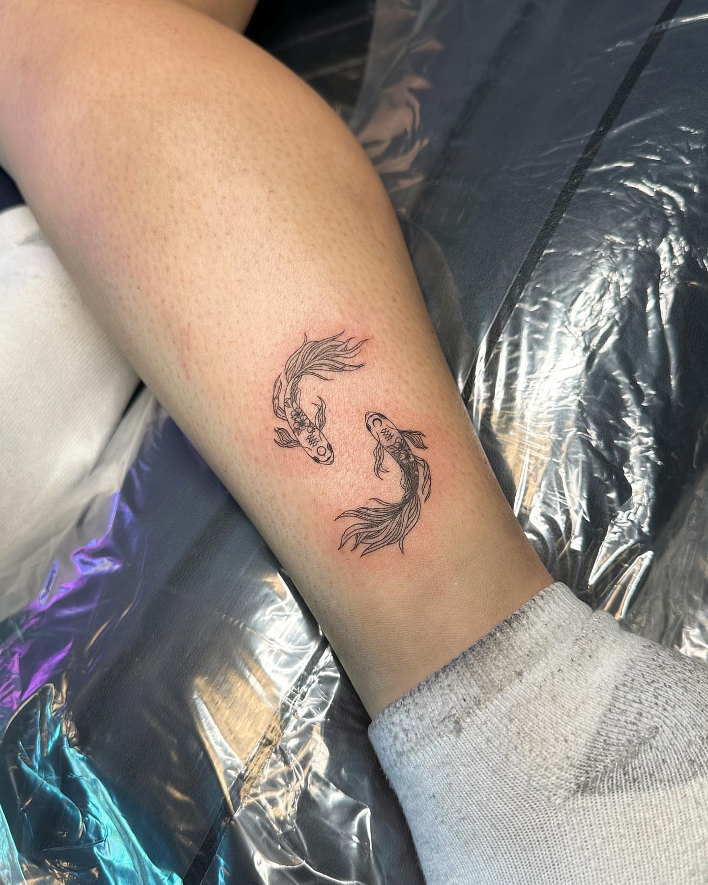 Two fish black and grey tattoo on the forearm by oc fine line & tiny tattoos