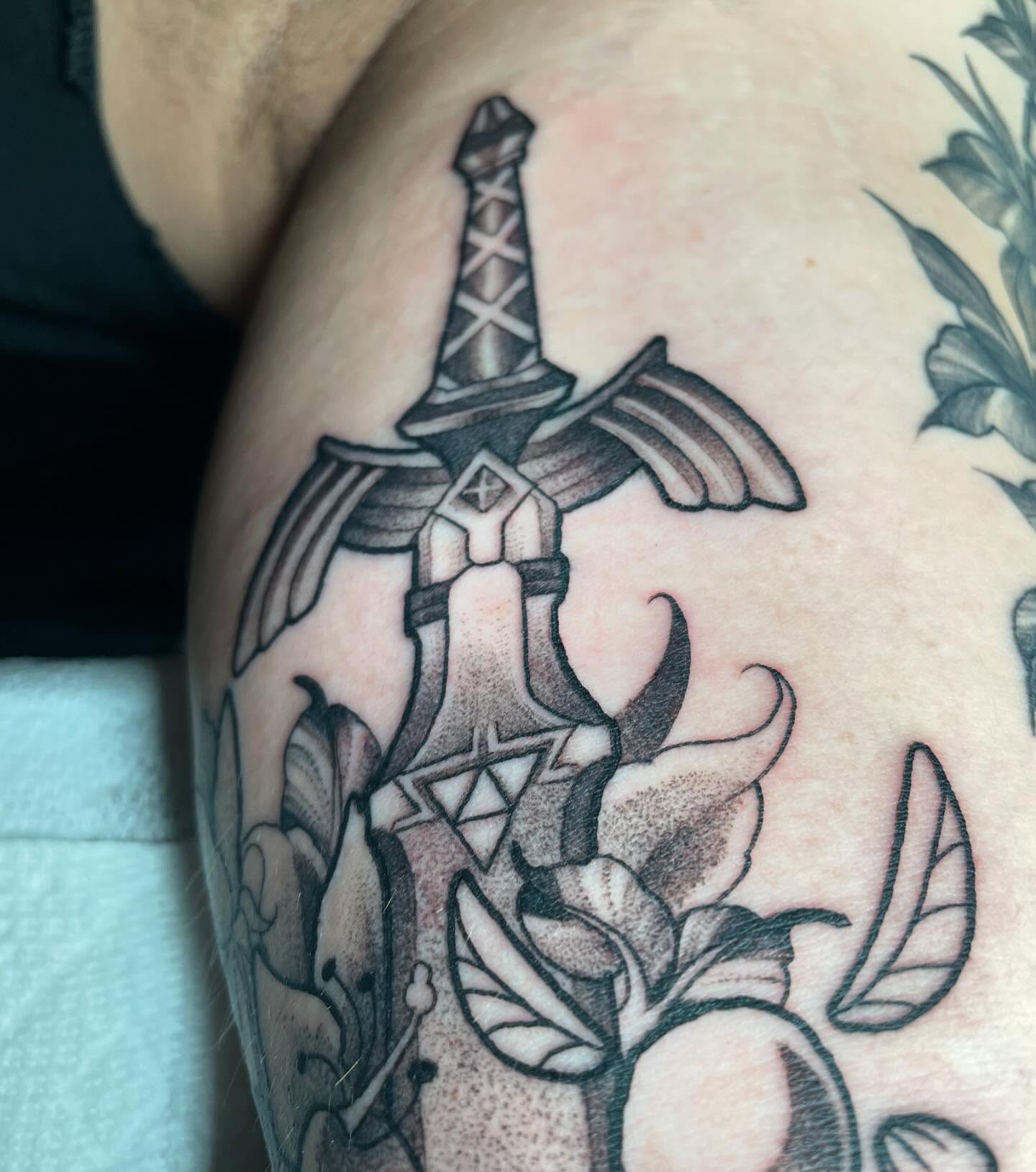 Sword and flower black and grey tattoo on the shoulder by Tayler Beetison