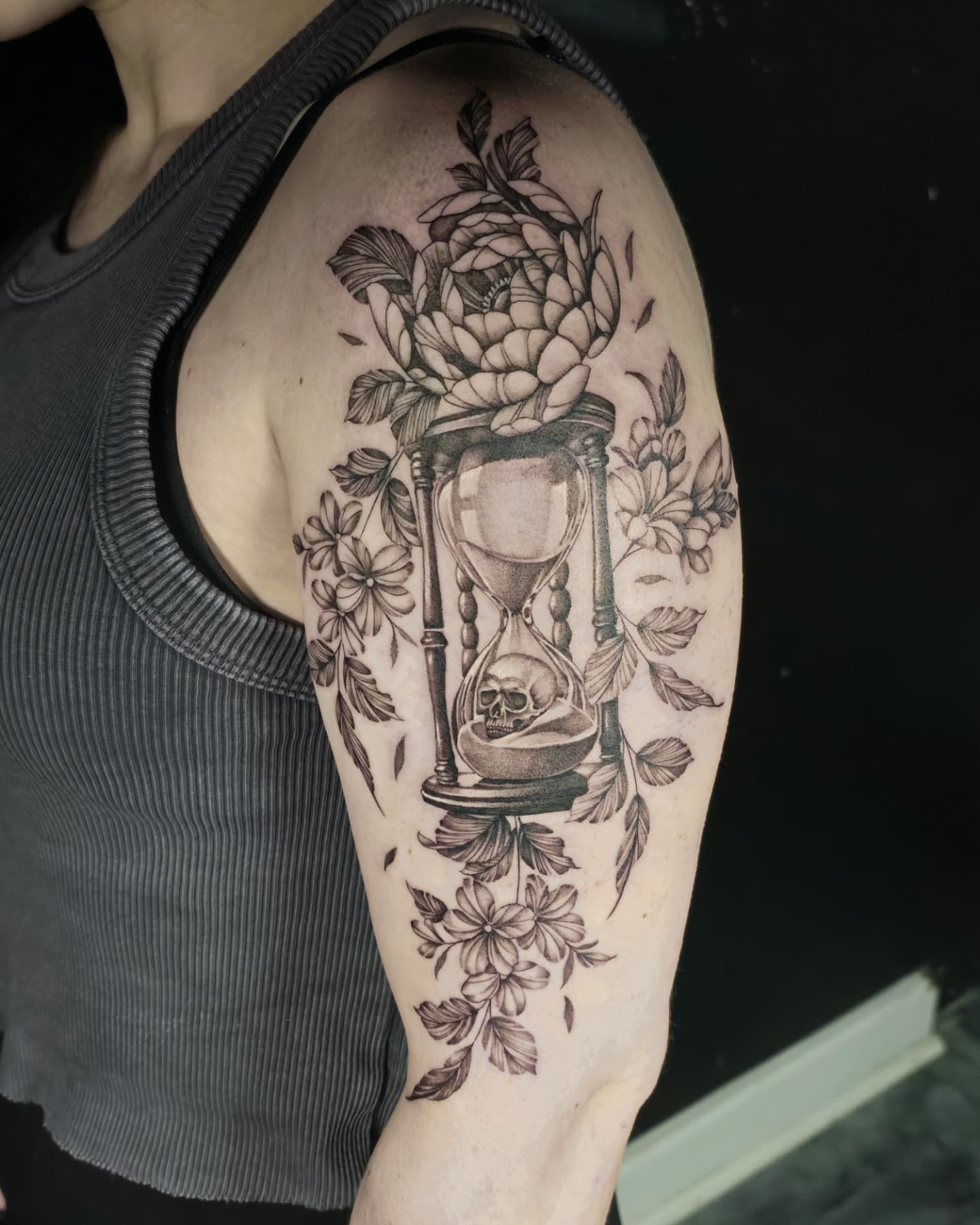 Hourglass with skull and flowers realism tattoo on the shoulder by Jake Barney
