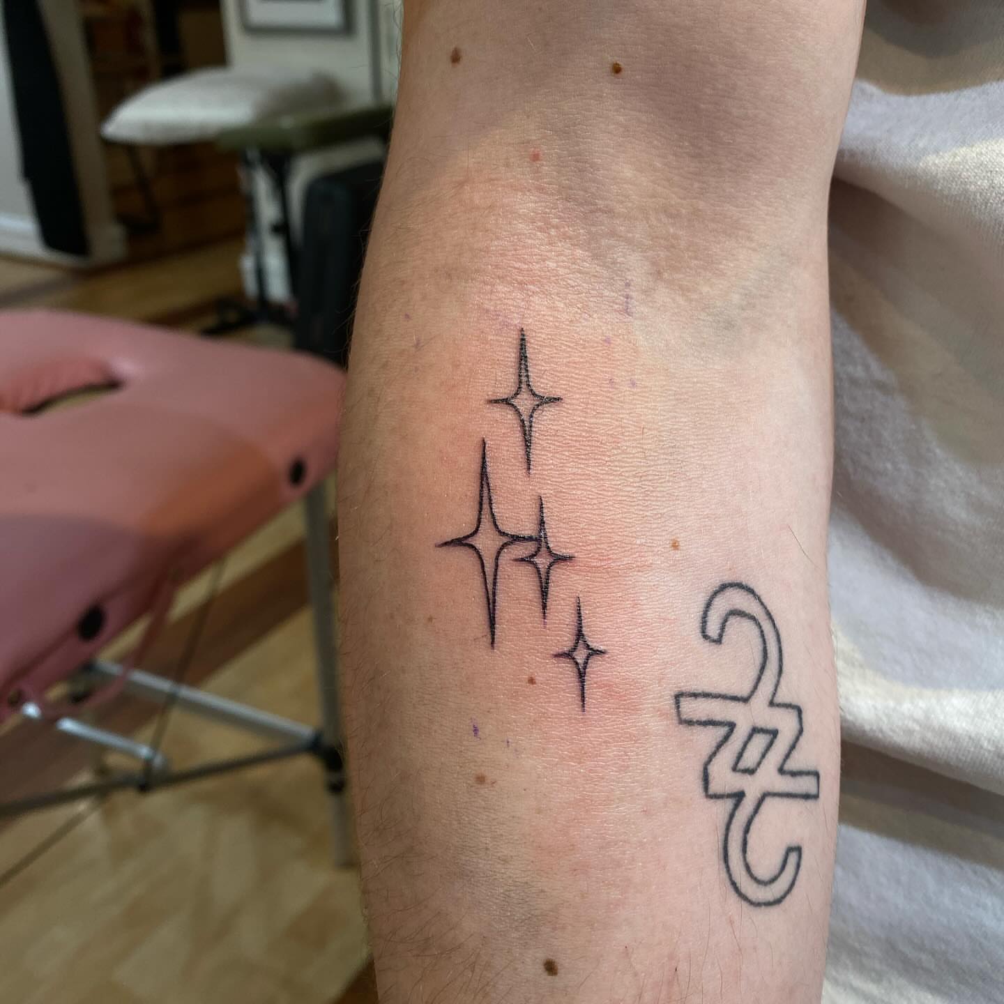 Stars and zodiac symbol fine line tattoo on the forearm by Leah Hammes