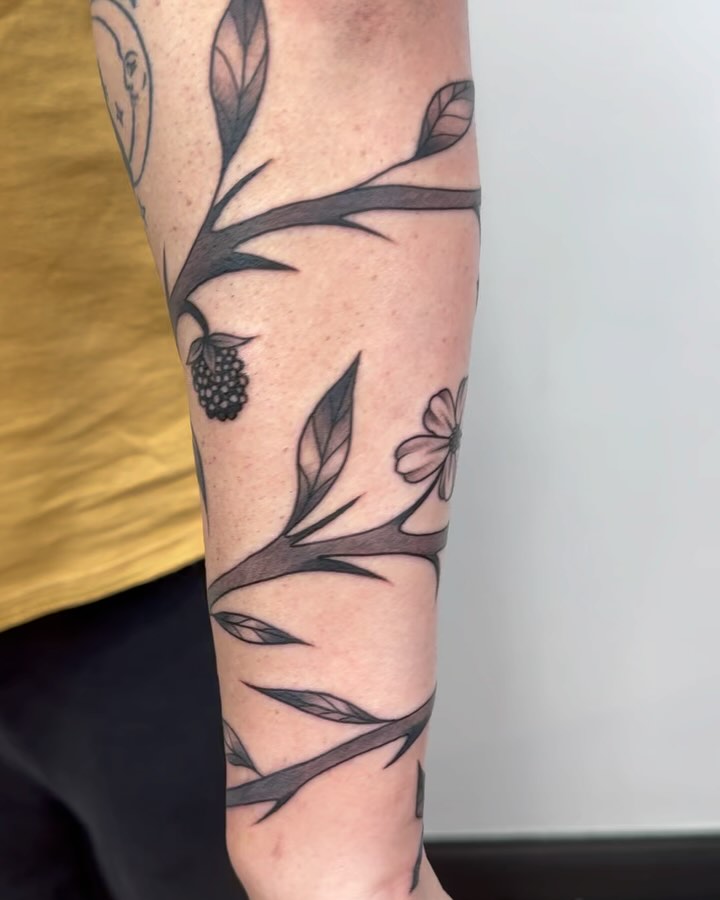 Branch with flowers and berries black and grey tattoo on the forearm by Makayla Dupre