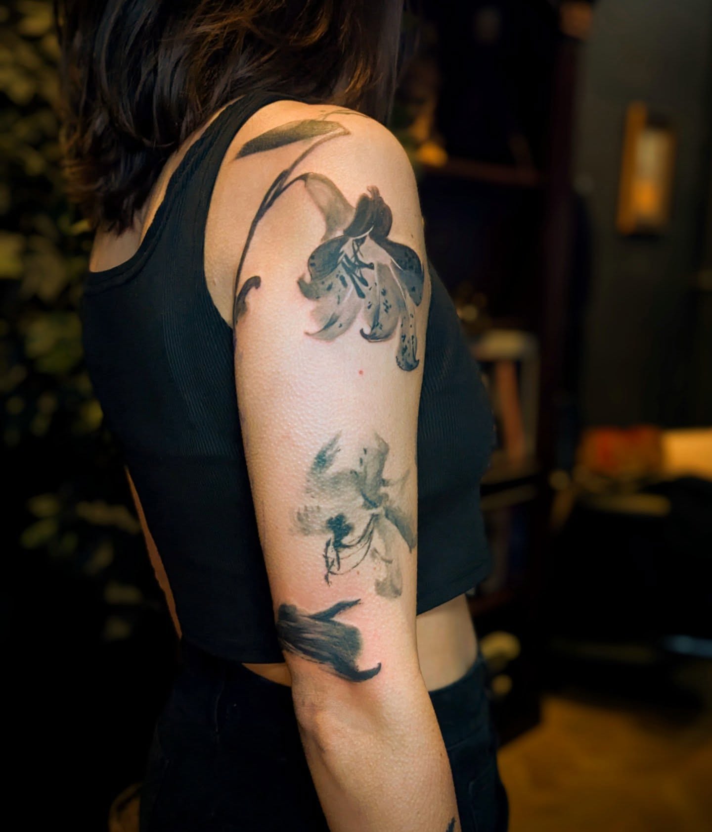 Lily watercolor tattoo on the upper arm by Jhenn