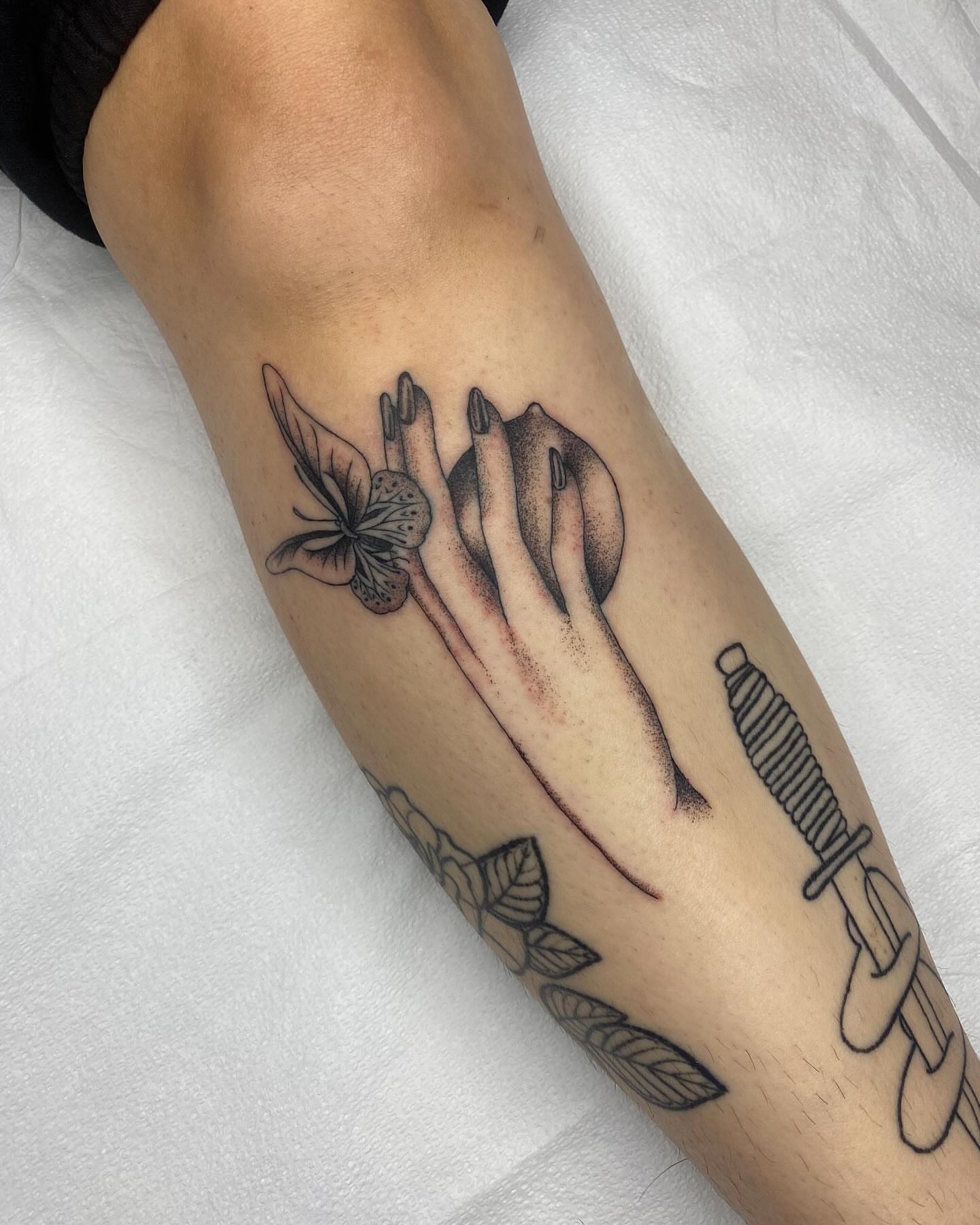 Hand with apple and butterfly dotwork tattoo on the forearm by Finley Jordan