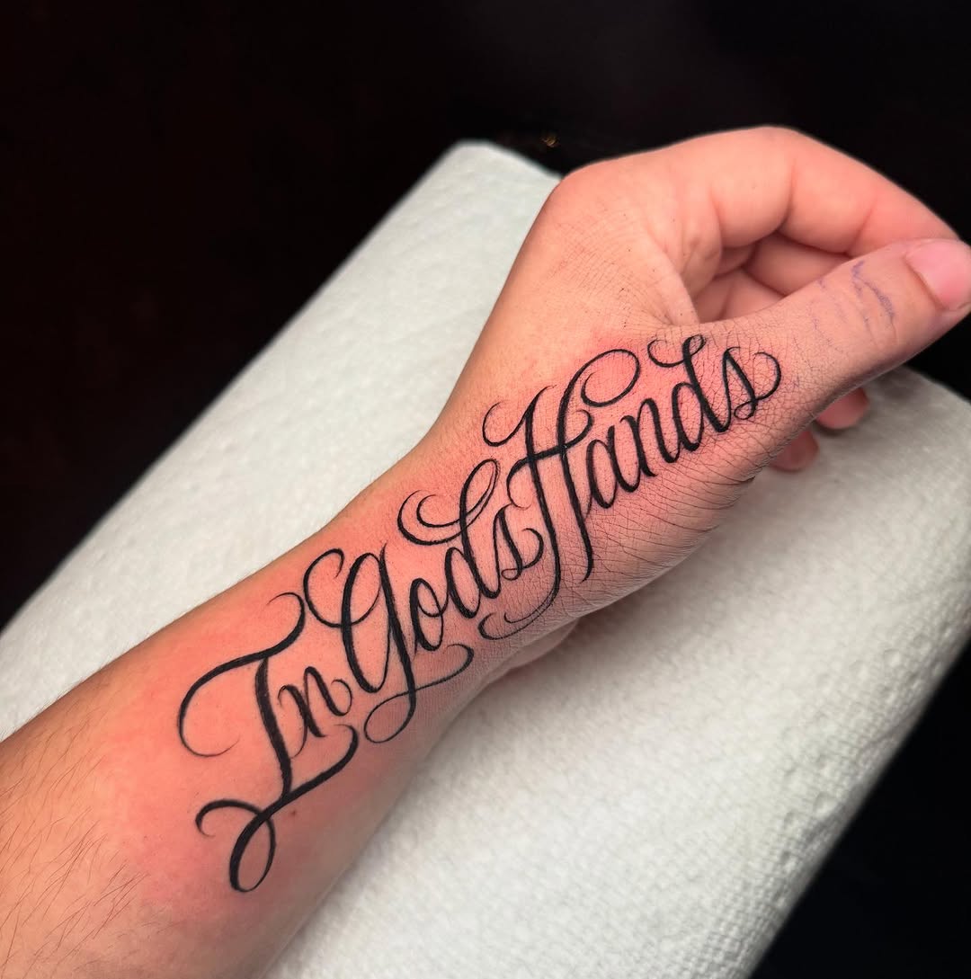 In God's Hands lettering lettering tattoo on the forearm by 𝕾𝖈𝖗𝖎𝖕𝖙 𝕾𝖕𝖊𝖈𝖎𝖆𝖑𝖎𝖘𝖙