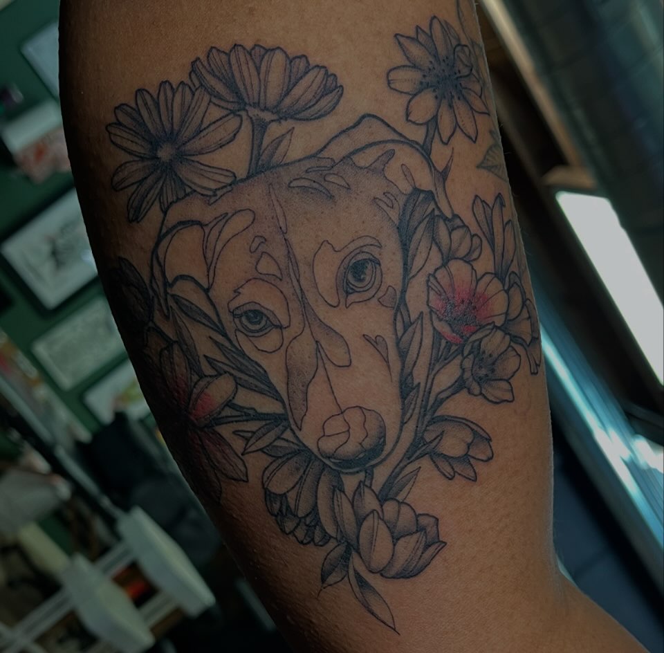Dog with flowers black and grey tattoo on the forearm by Dallas Davis