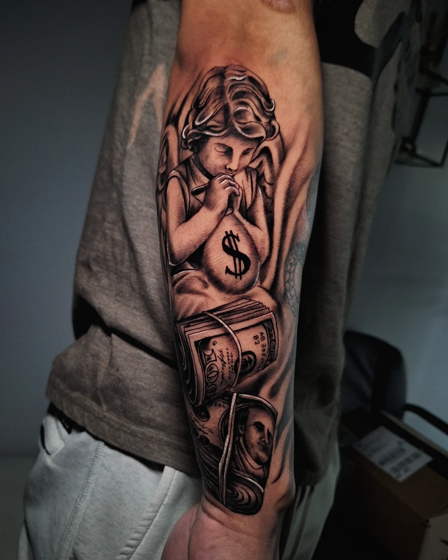 Praying angel with money bag realism tattoo on the forearm by Daero Tattoo, New York, New York