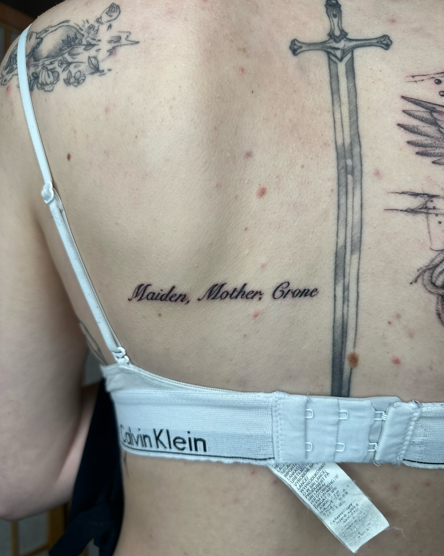 Three-word phrase black and grey tattoo on the back by cora cupid