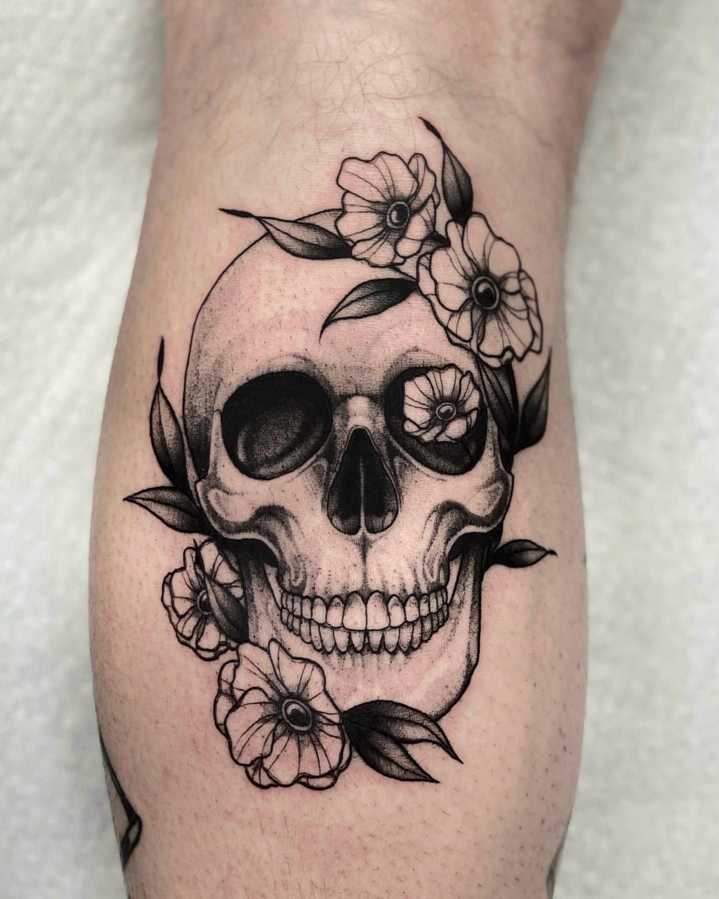 Skull with flowers realism tattoo on the forearm by jada