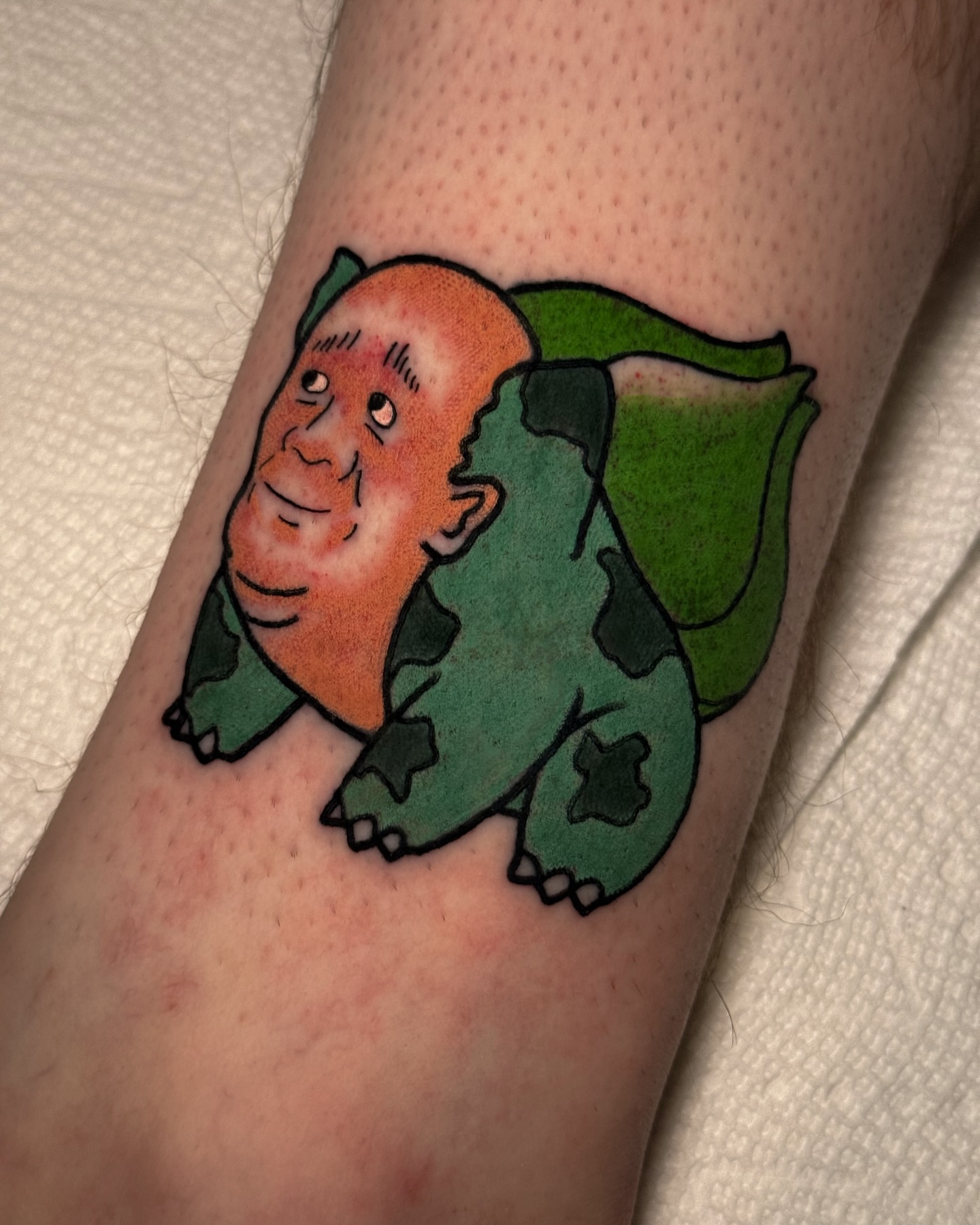 Man with green dinosaur illustrative tattoo on the forearm by Cory Cartwright