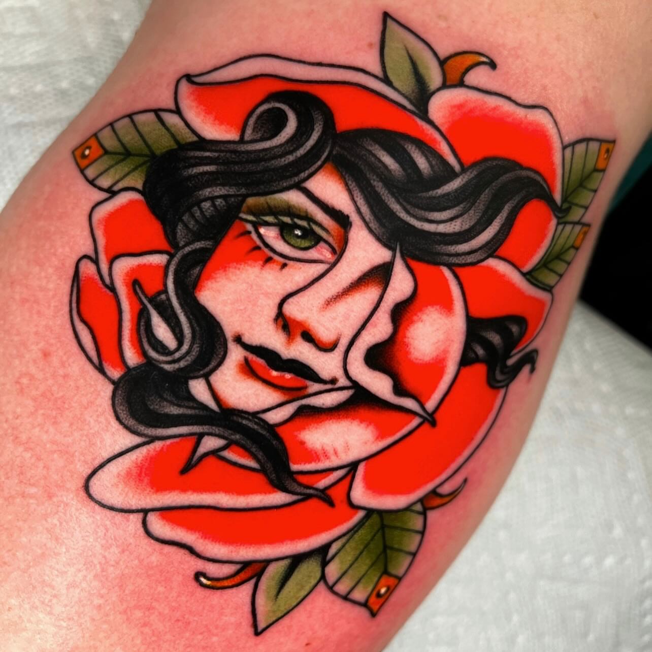 Woman's face within a rose American traditional tattoo on the forearm by Hailey Johnson