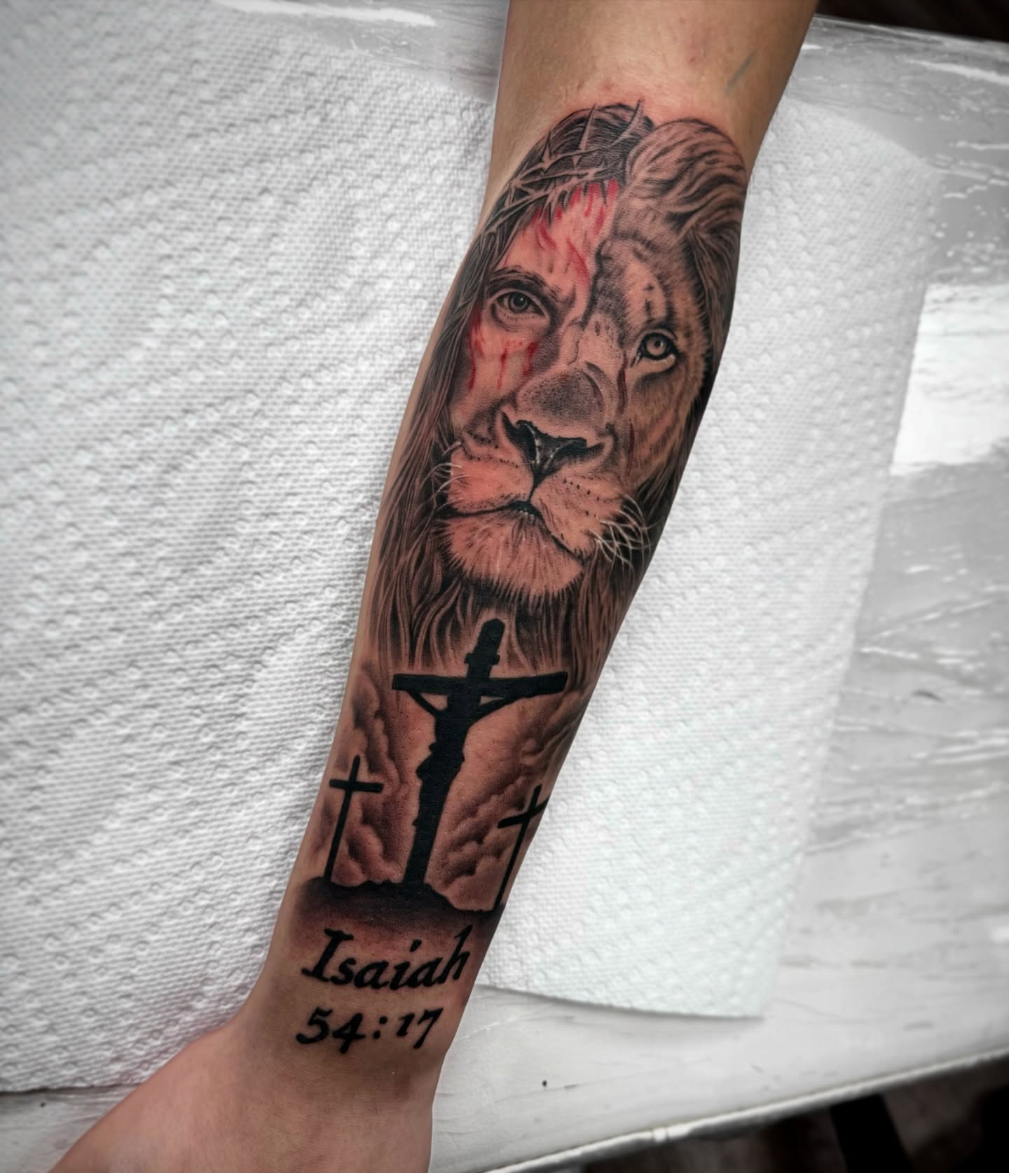 Lion and crucifix realism tattoo on the forearm by Mike Hudson