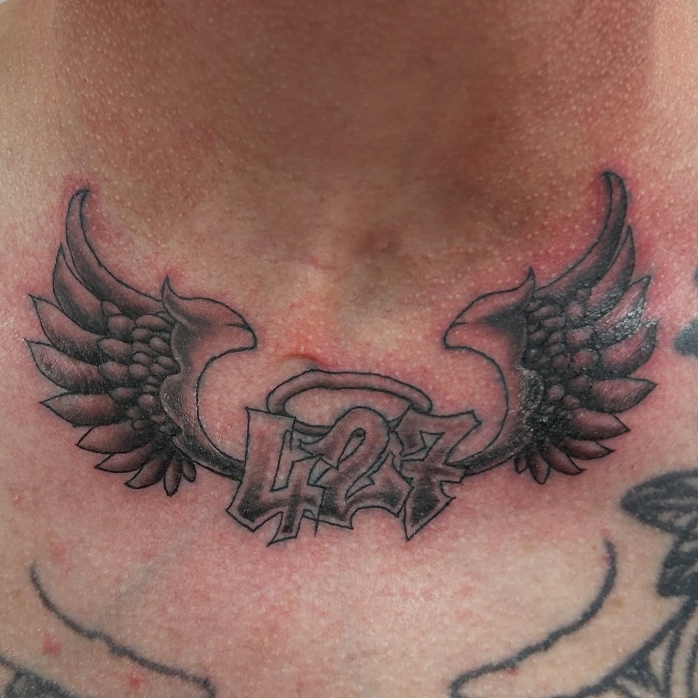 Wings and number black and grey tattoo on the chest by Sean OHara