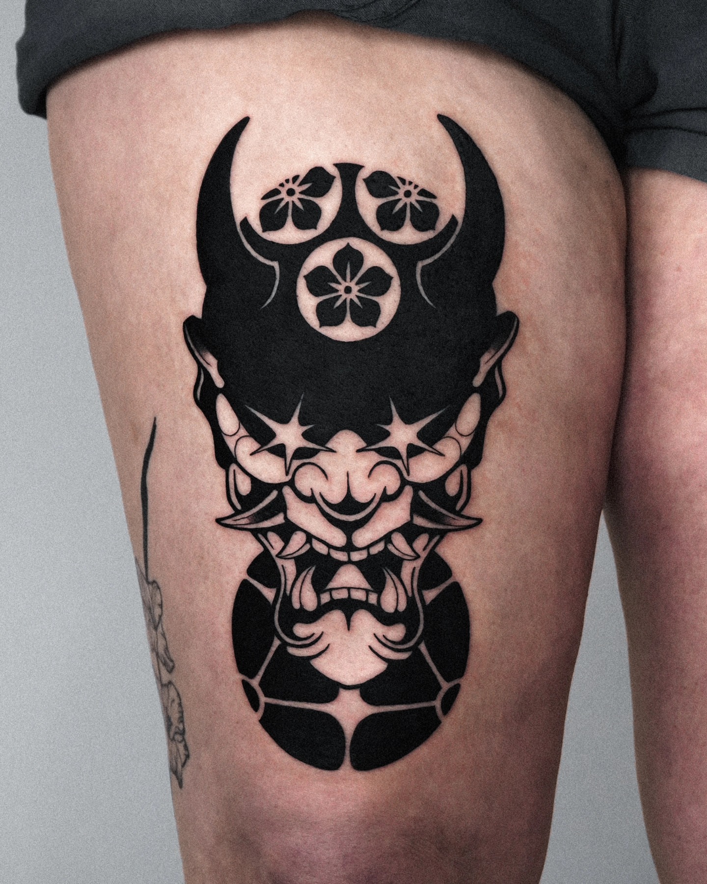 Demon mask black and grey tattoo on the thigh by Jeremy "Jerms" Camposanto