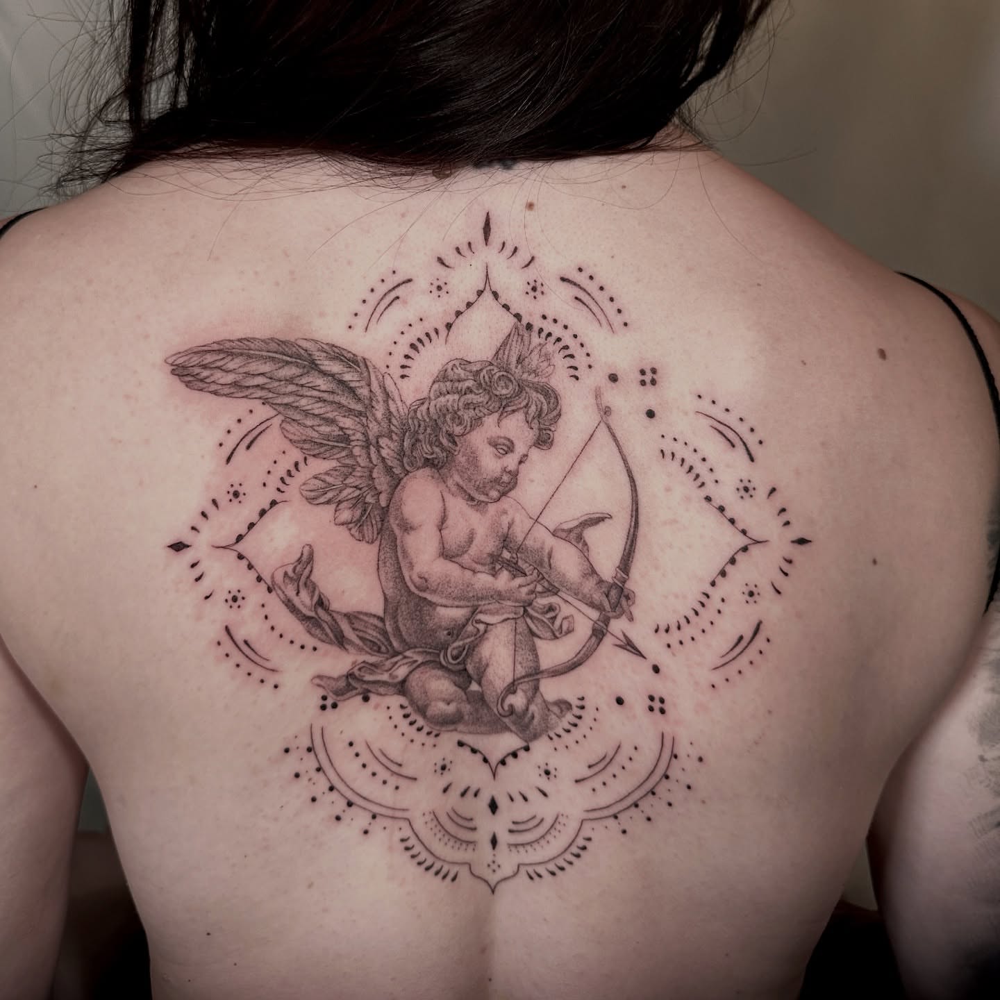 Cherub with bow black and grey tattoo on the back by Rachel