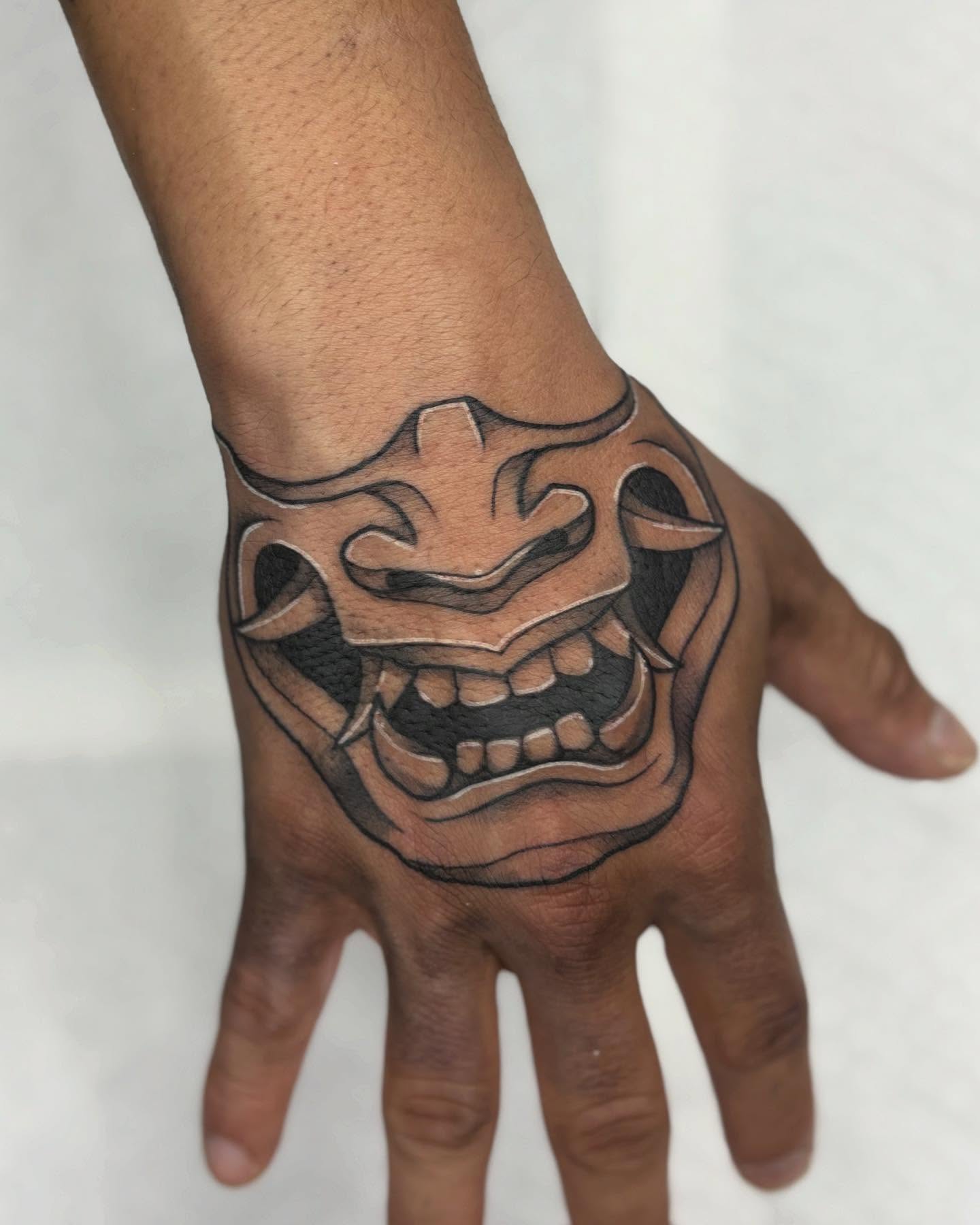 Mask black and grey tattoo on the hand by Tattoos by Tessa