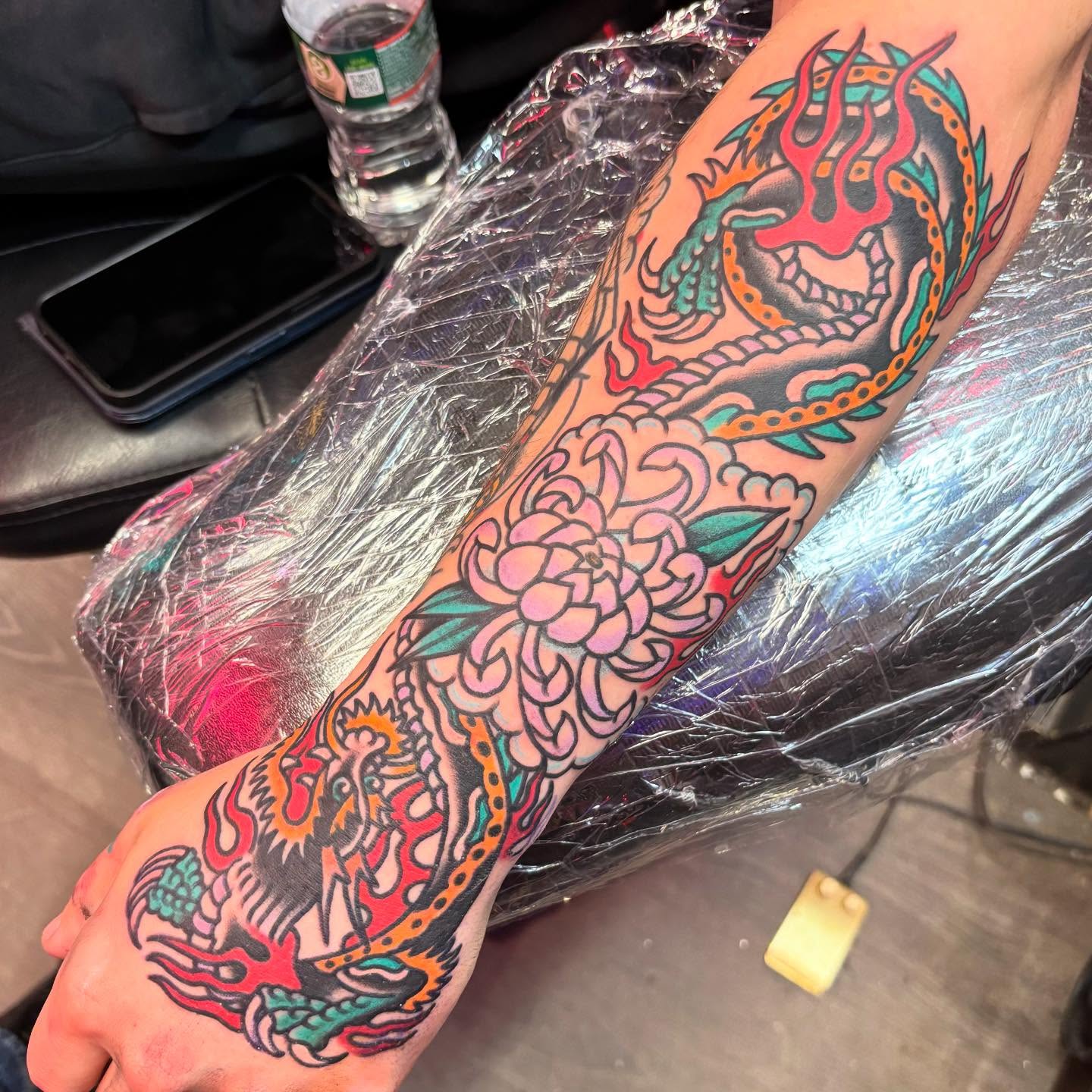 Dragon and chrysanthemum American traditional tattoo on the forearm by @dannydoestattoos