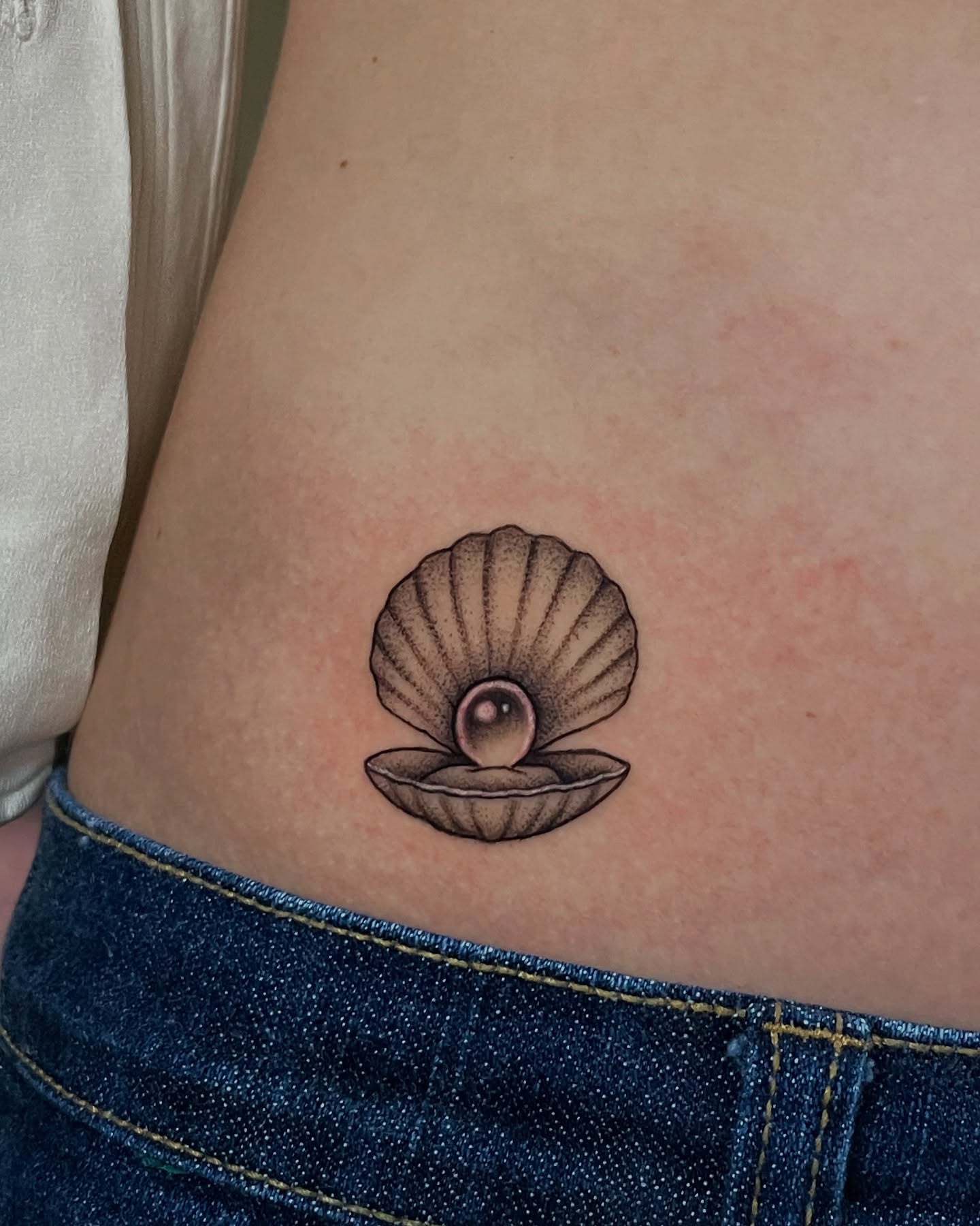 Shell with pearl realism tattoo on the ribs by Candence Smith