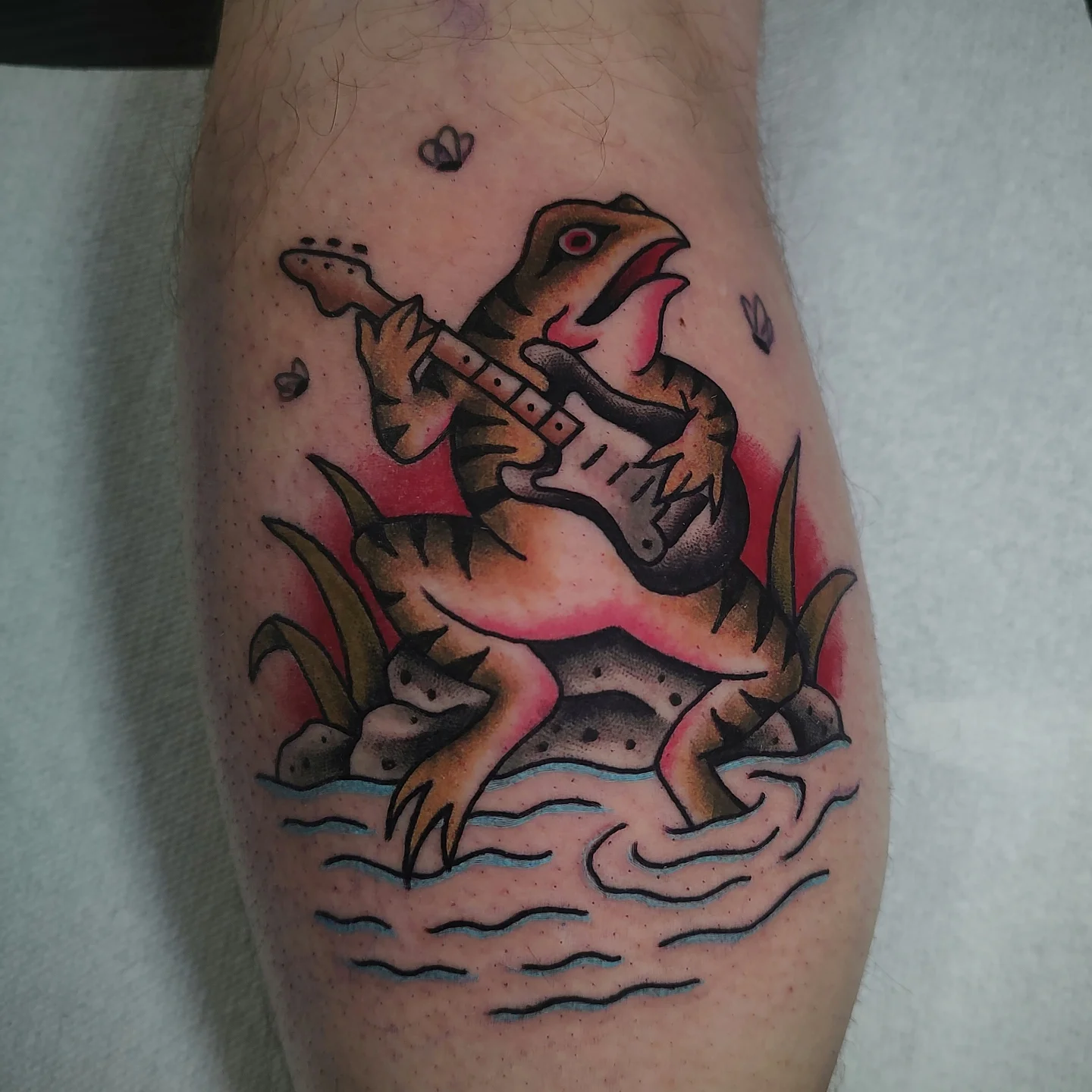 Dinosaur playing guitar American traditional tattoo on the forearm by Hope Higgins