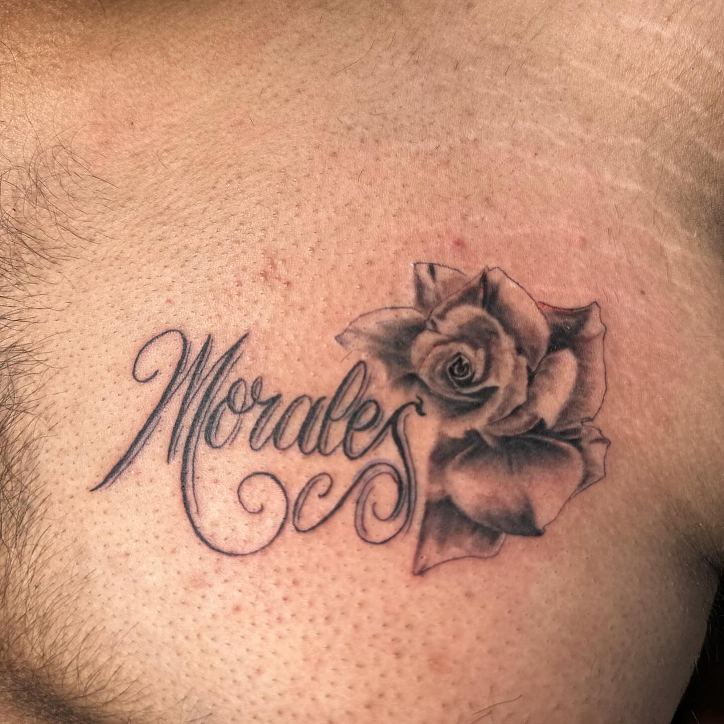 Rose and cursive text black and grey tattoo on the chest by Devin