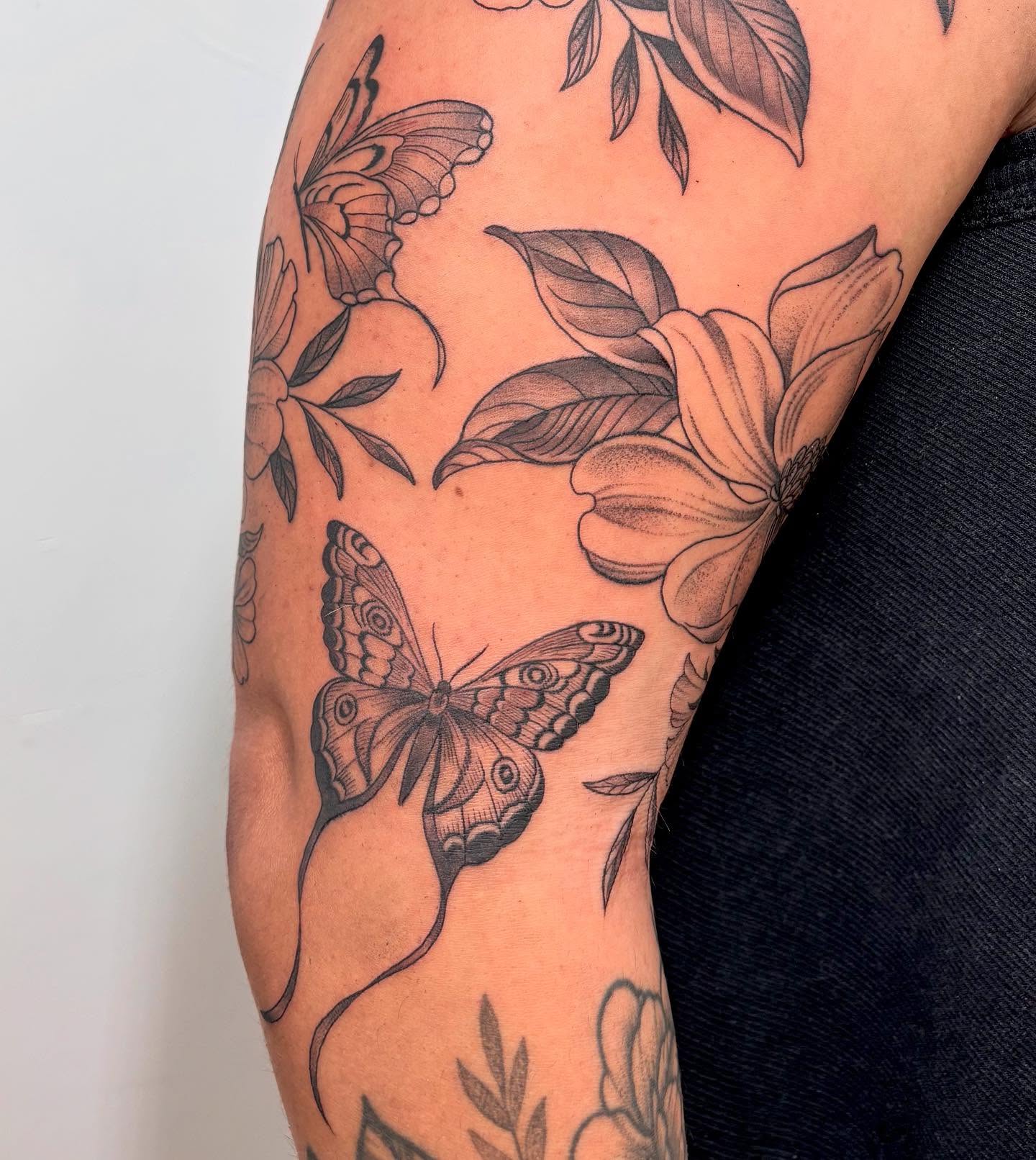 Butterfly and flowers black and grey tattoo on the forearm by Kinsey Miller