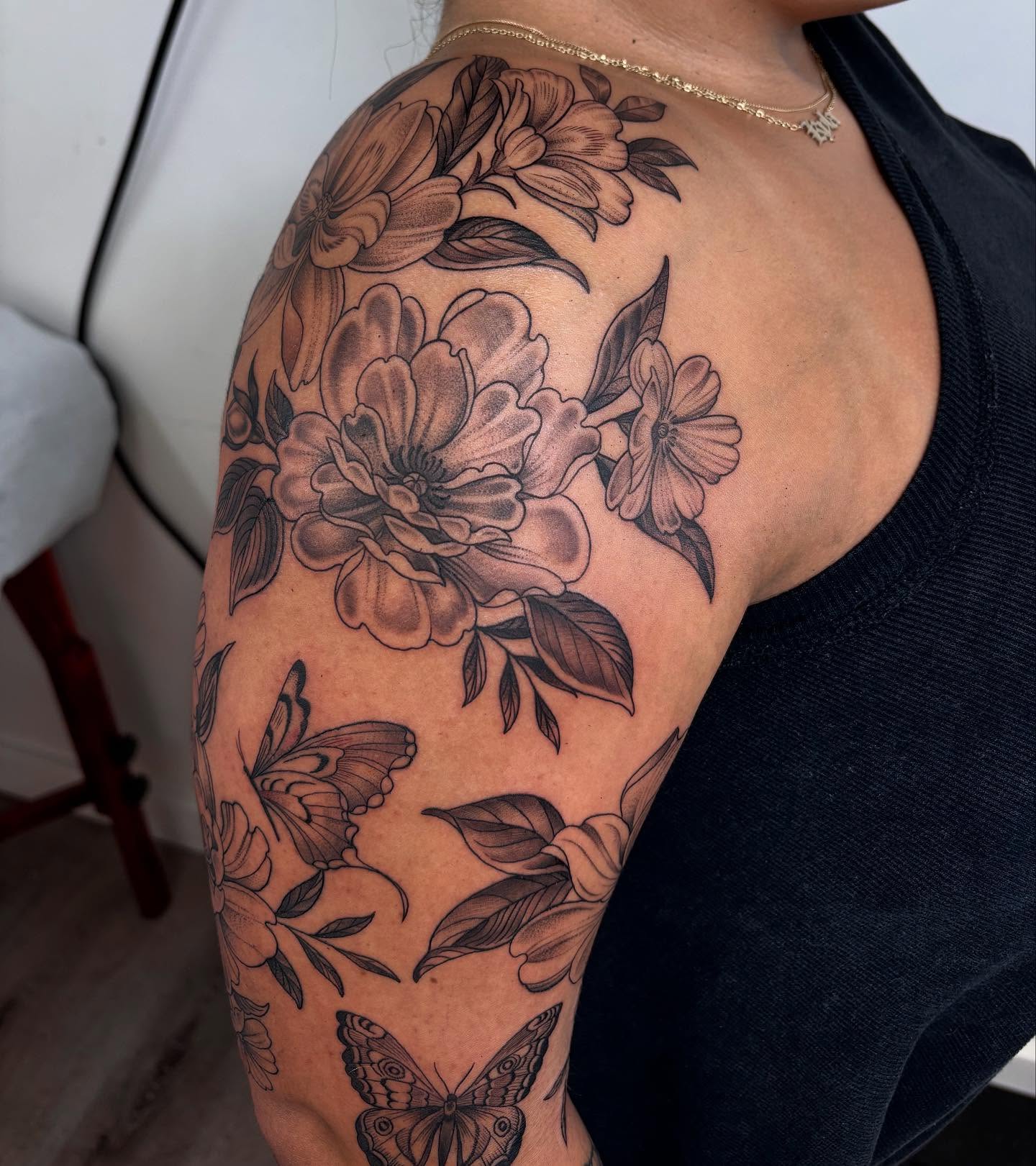 Flowers and butterflies black and grey tattoo on the upper arm by Kinsey Miller