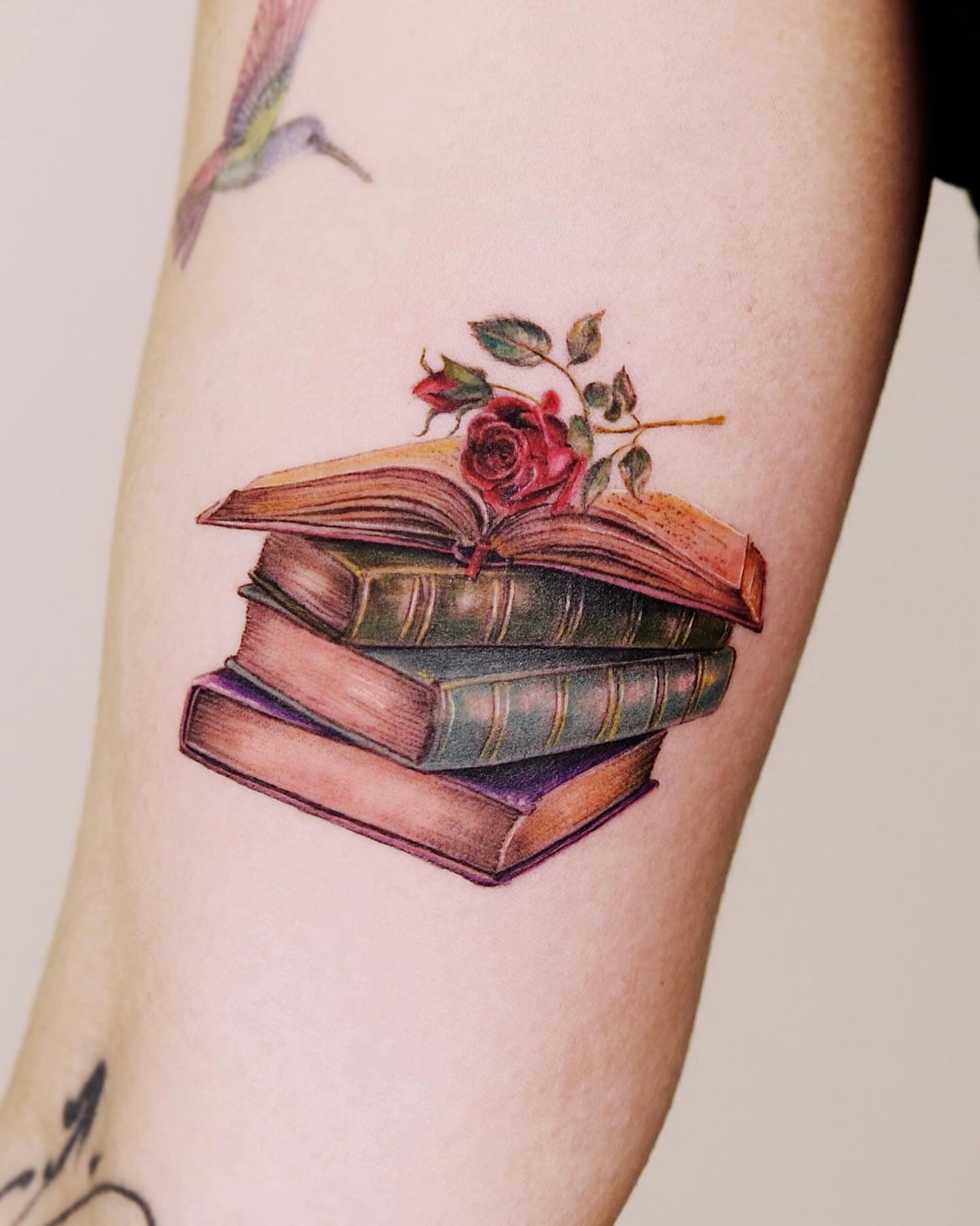 Stack of books with rose realism tattoo on the forearm by Yeye