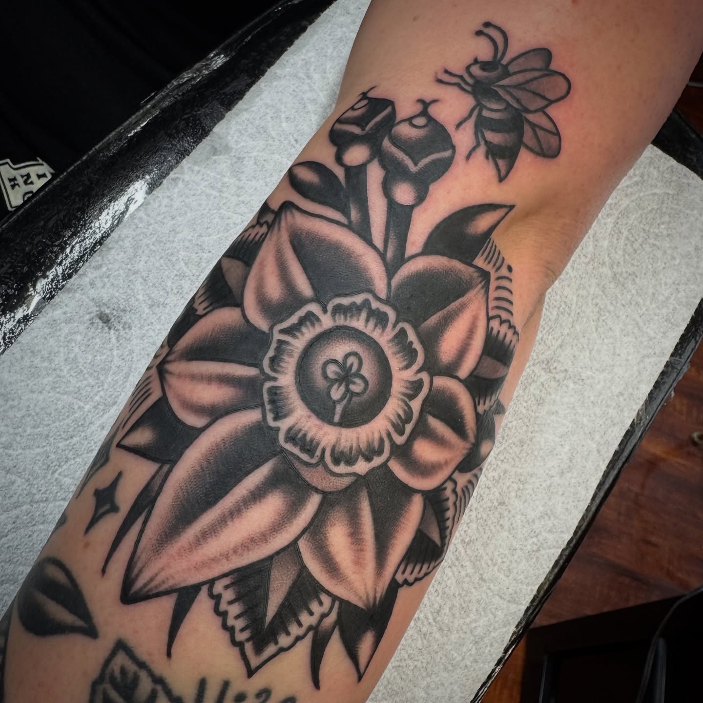 Daffodil and bee American traditional tattoo on the forearm by Rogelio Robles