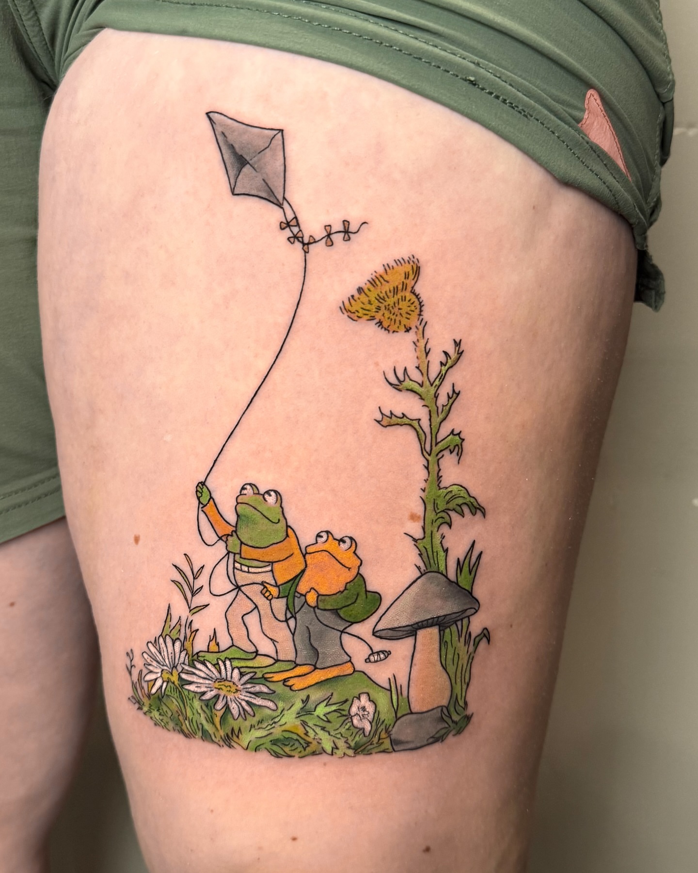 Frog characters flying kite illustrative tattoo on the thigh by Demi DiMartino