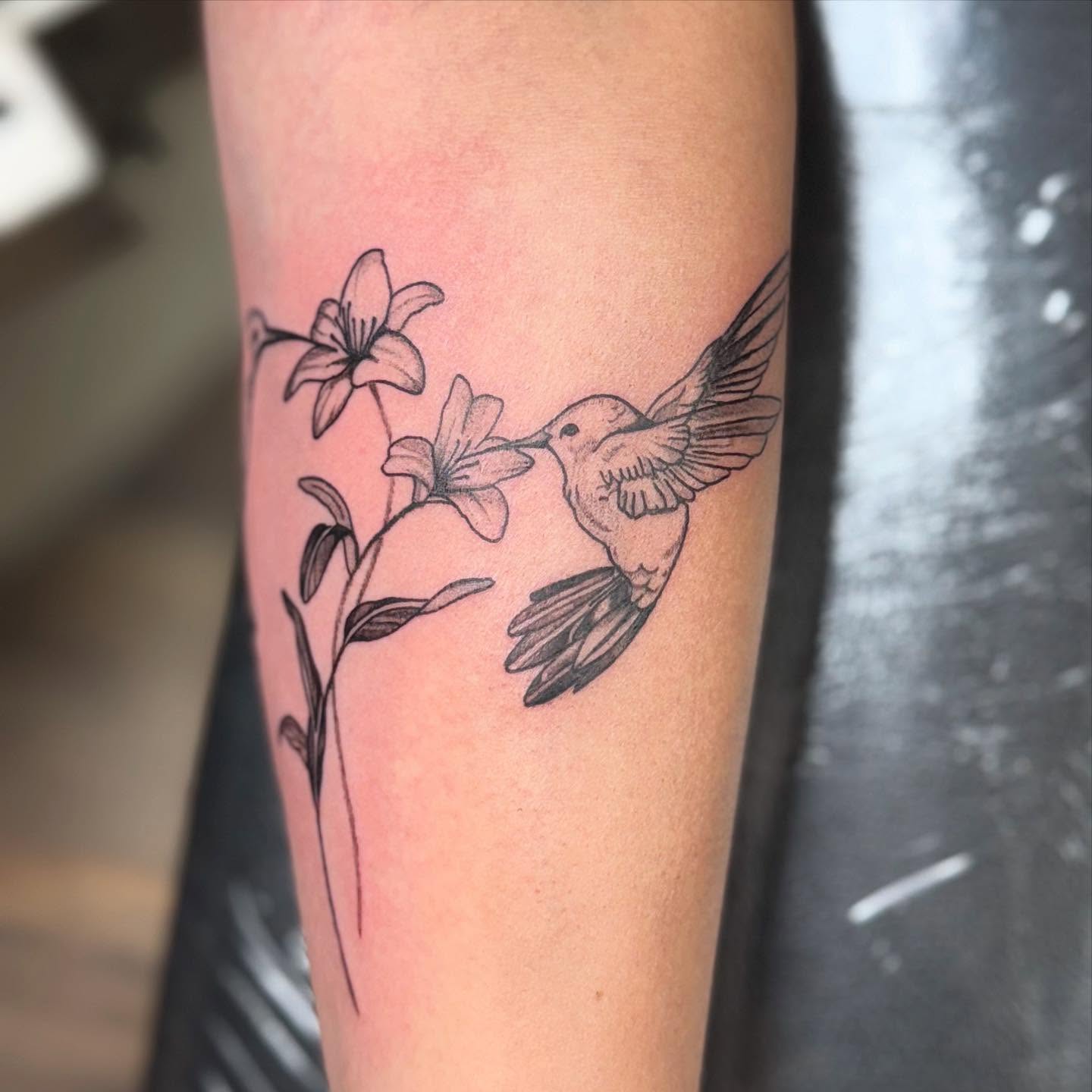 Hummingbird and lilies black and grey tattoo on the forearm by Mickey
