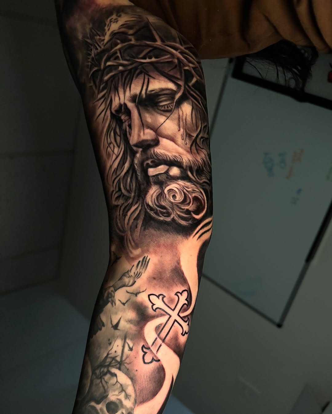 Jesus Christ, cross, skull, birds Chicano tattoo on the forearm by Eric Garcia