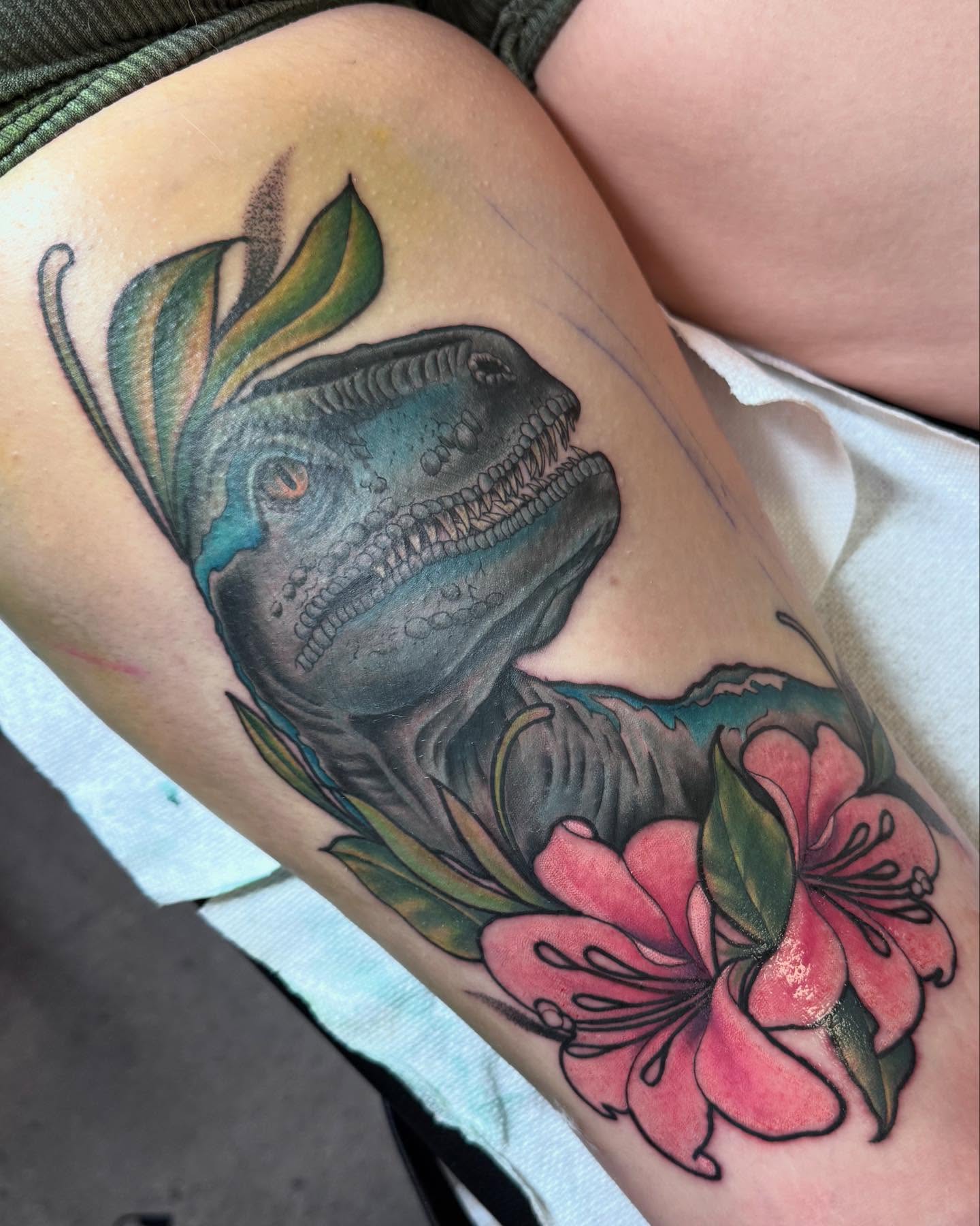 Dinosaur and flowers realism tattoo on the thigh by Stephanie Cruz, Kansas City, Missouri