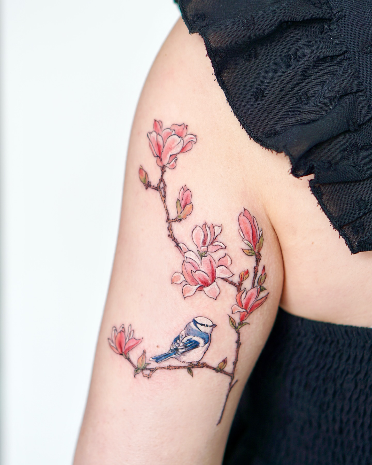 Magnolia blossoms and bird realism tattoo on the upper arm by Isle