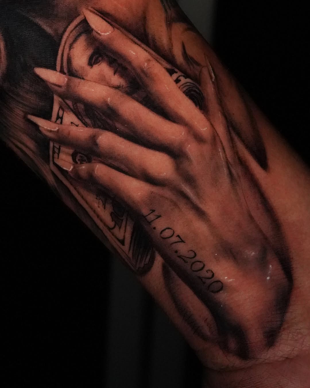 Hand holding money with date Chicano tattoo on the forearm by Jennifer Garcia