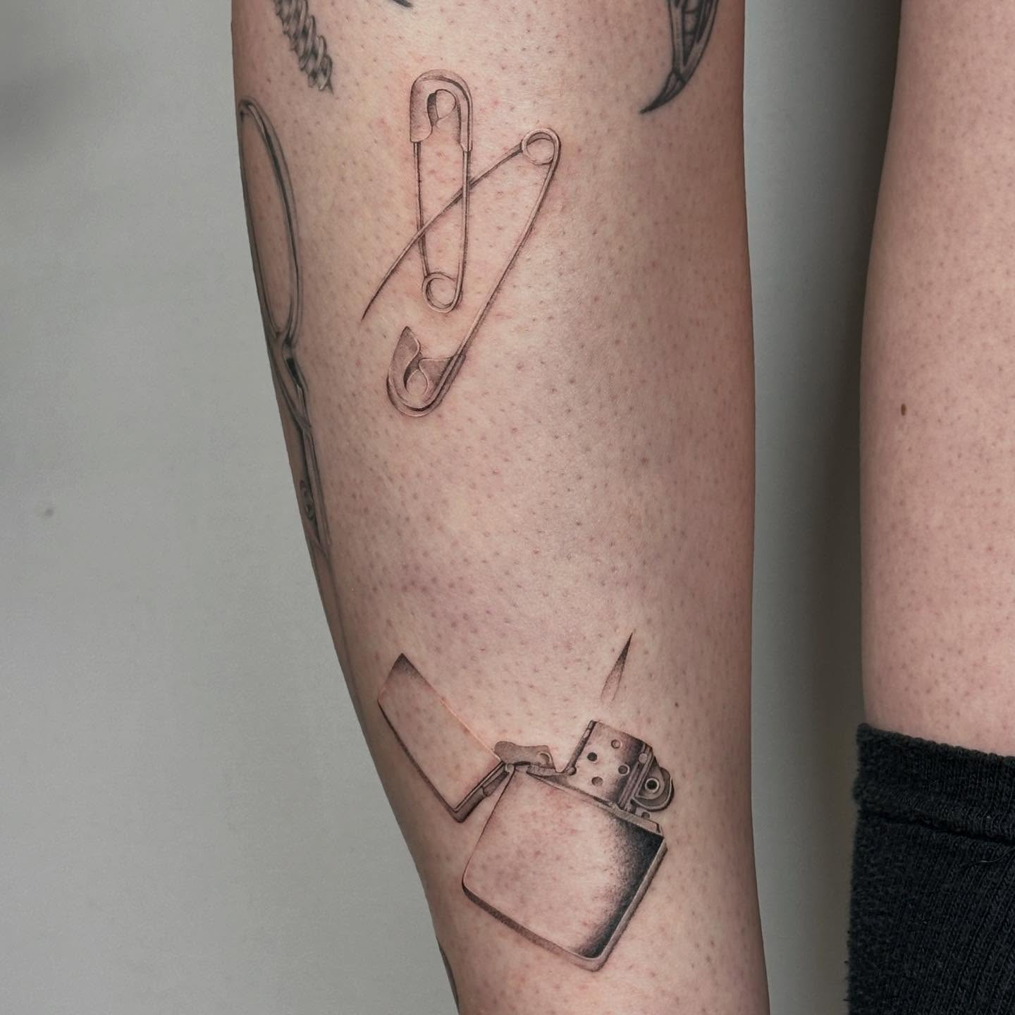 Safety pin and lighter black and grey tattoo on the forearm by ๐๐๐๐ ๐๐๐๐