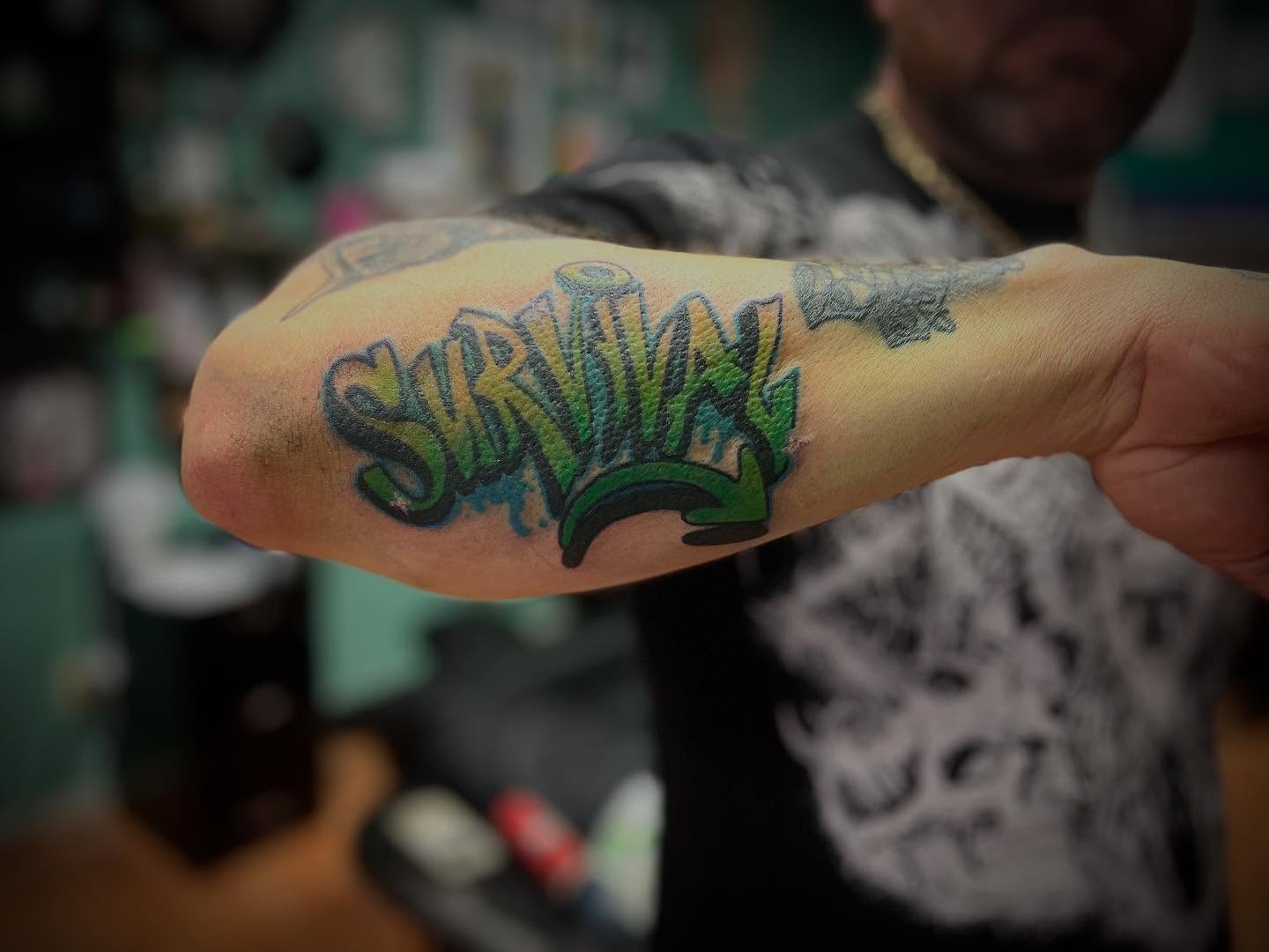 Survival lettering script tattoo on the forearm by Katie Sayre