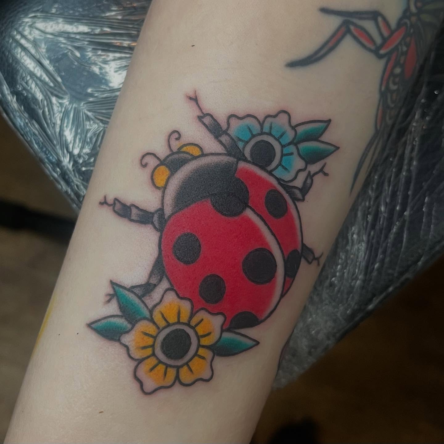 Ladybug and flowers American traditional tattoo on the forearm by Mariah Nguyen