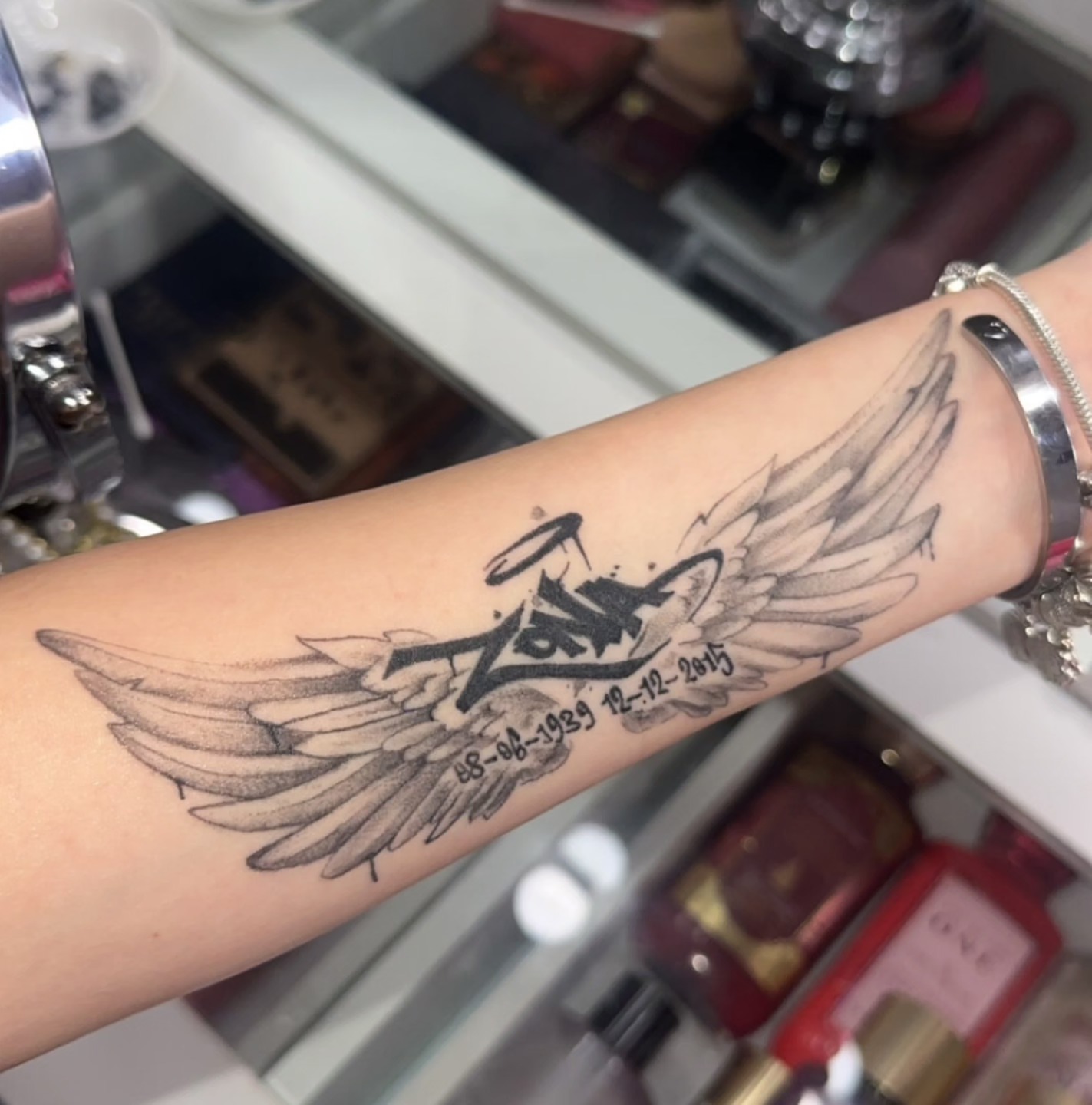 Wings and date black and grey tattoo on the forearm by Hot Dawg