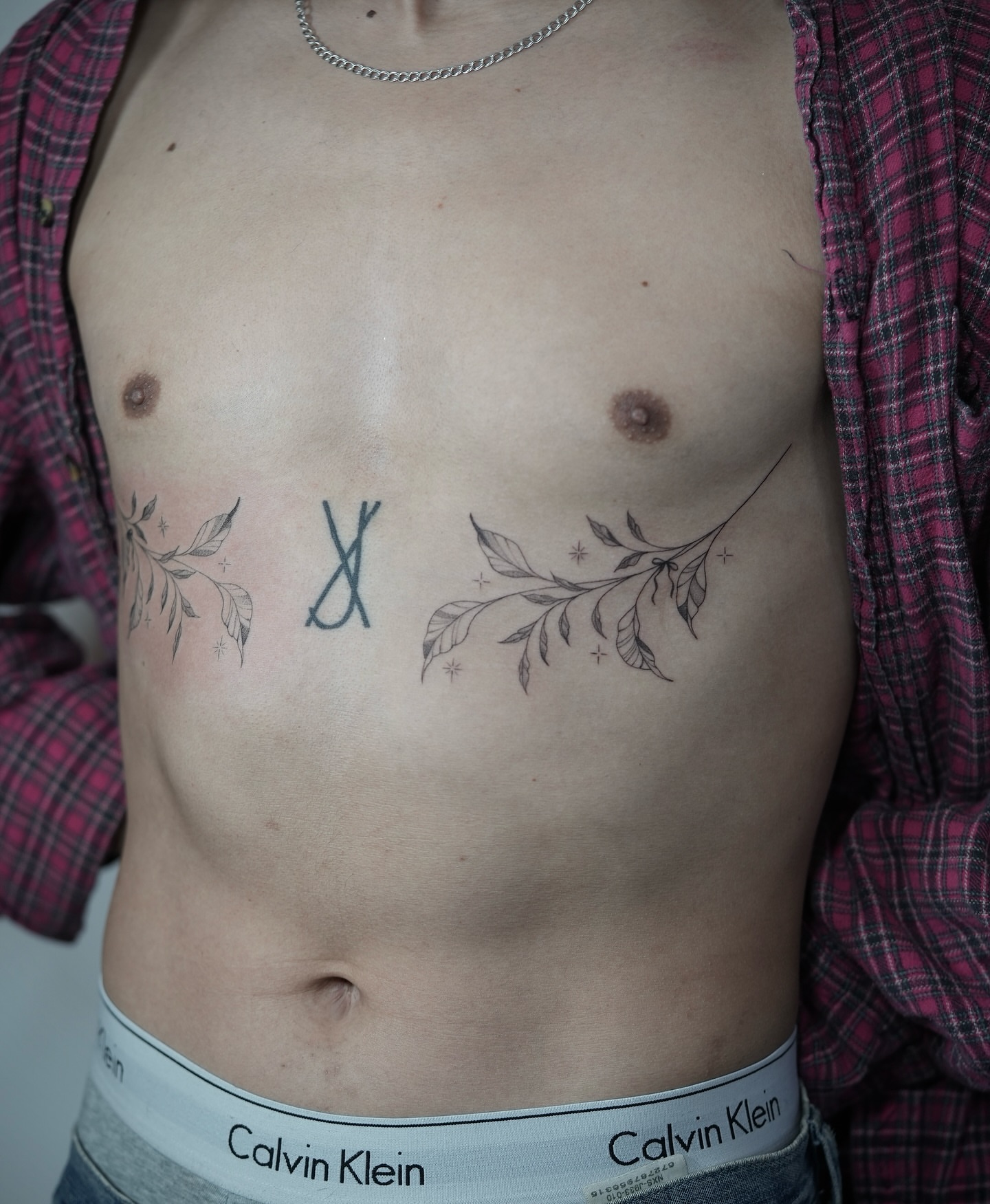 Cross and leaves black and grey tattoo on the chest by Jennifer Fuster