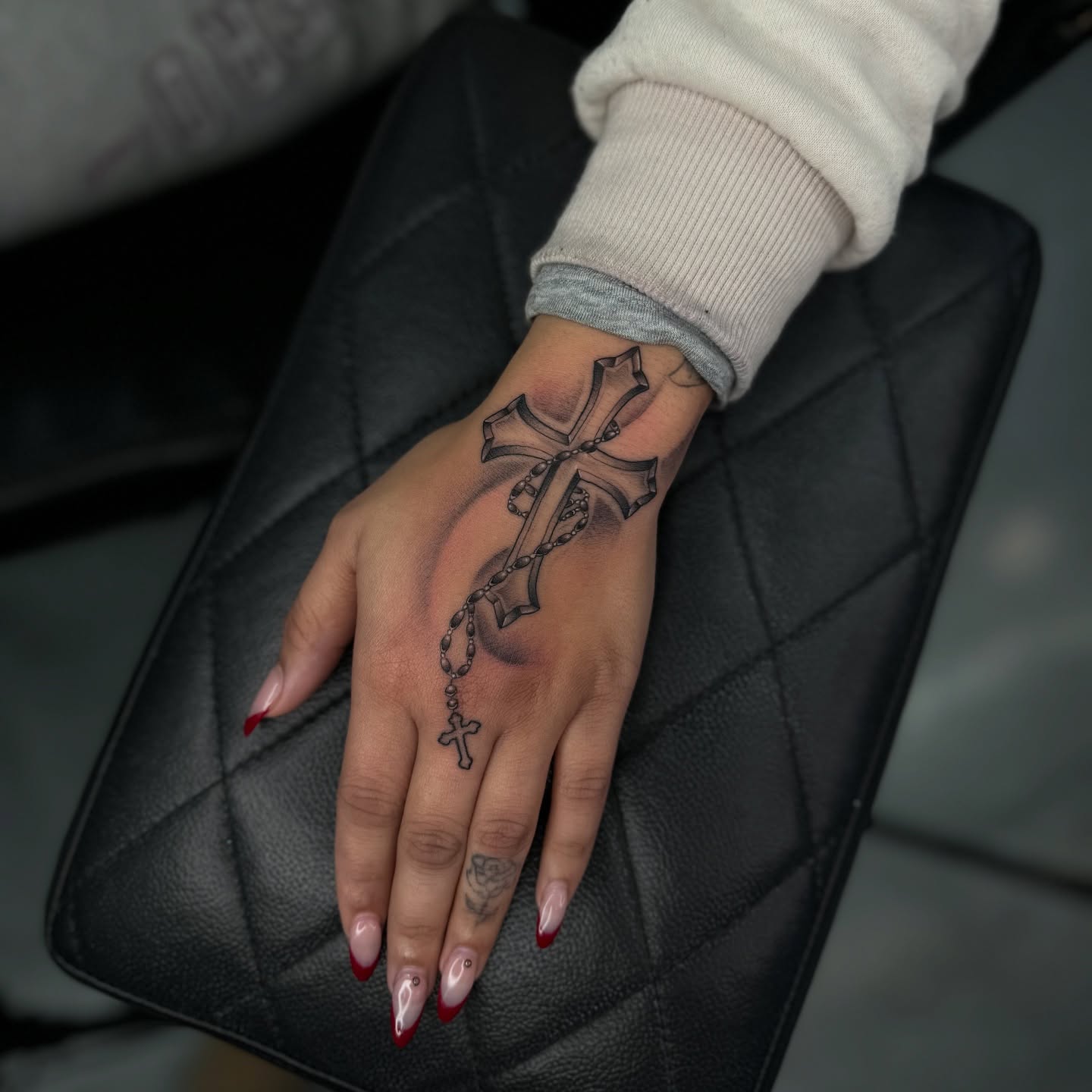 Cross with rosary black and grey tattoo on the hand by Steph π€