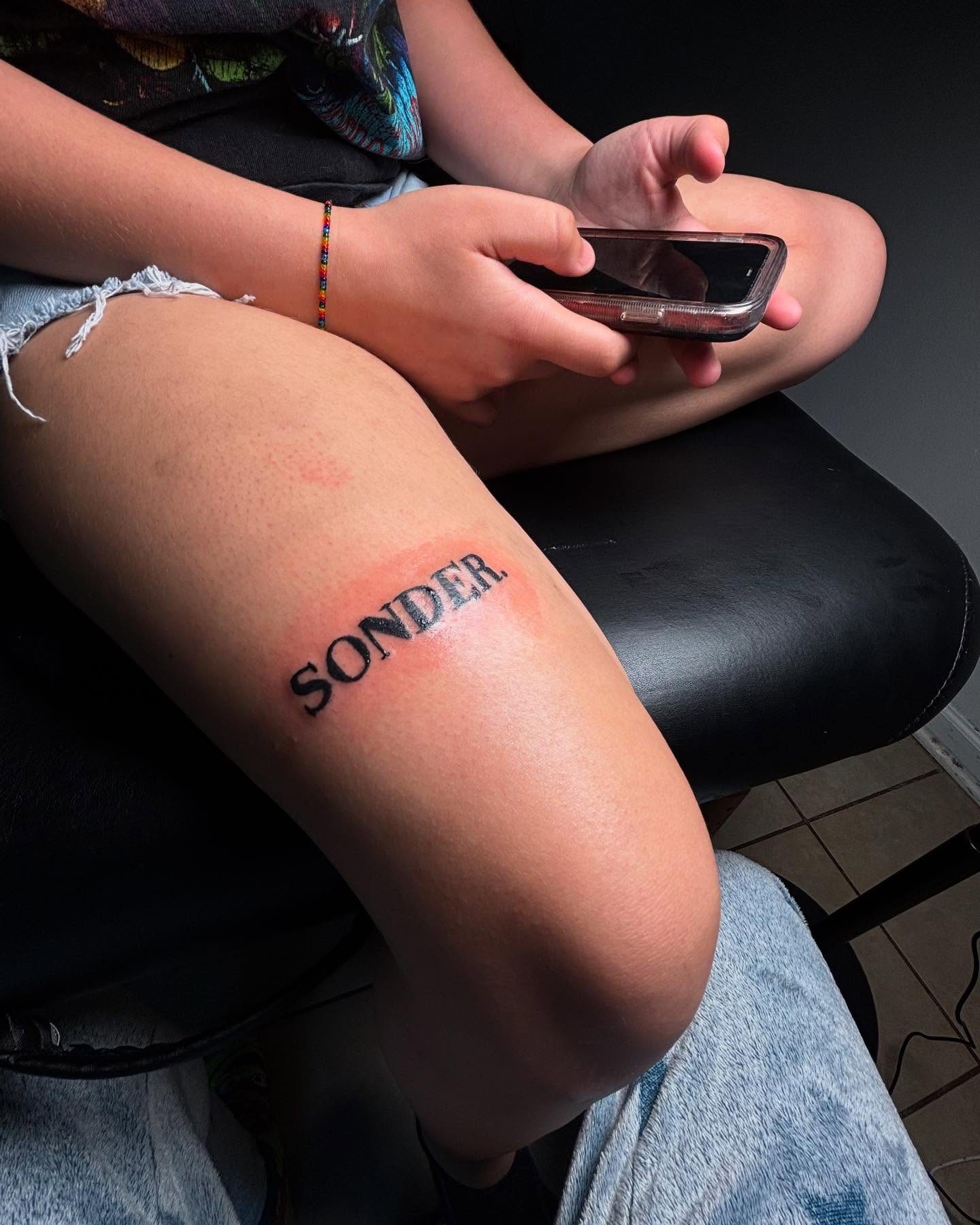SONDER lettering script tattoo on the thigh by Mc X Happo