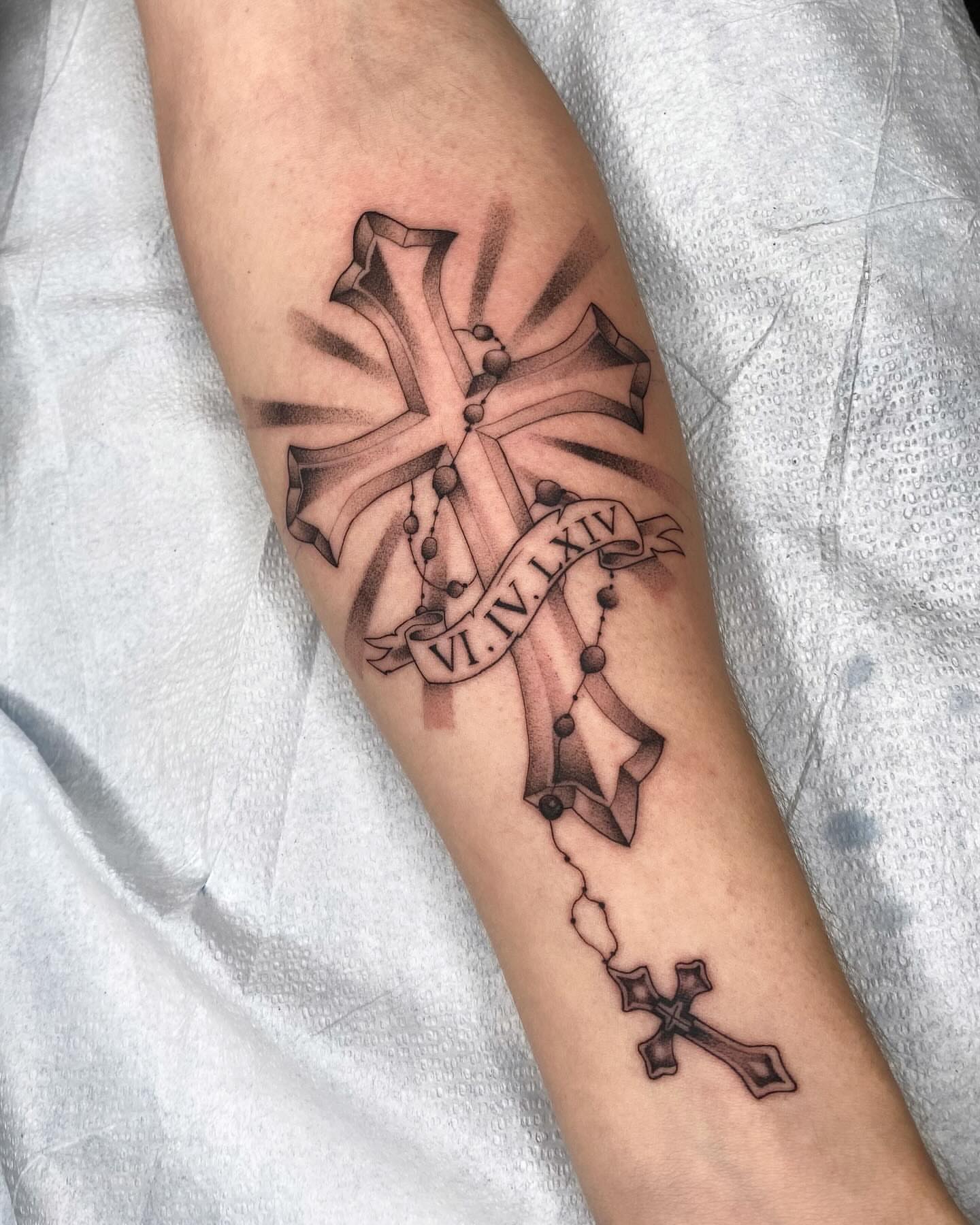 Cross and rosary black and grey tattoo on the forearm by Cody Mason