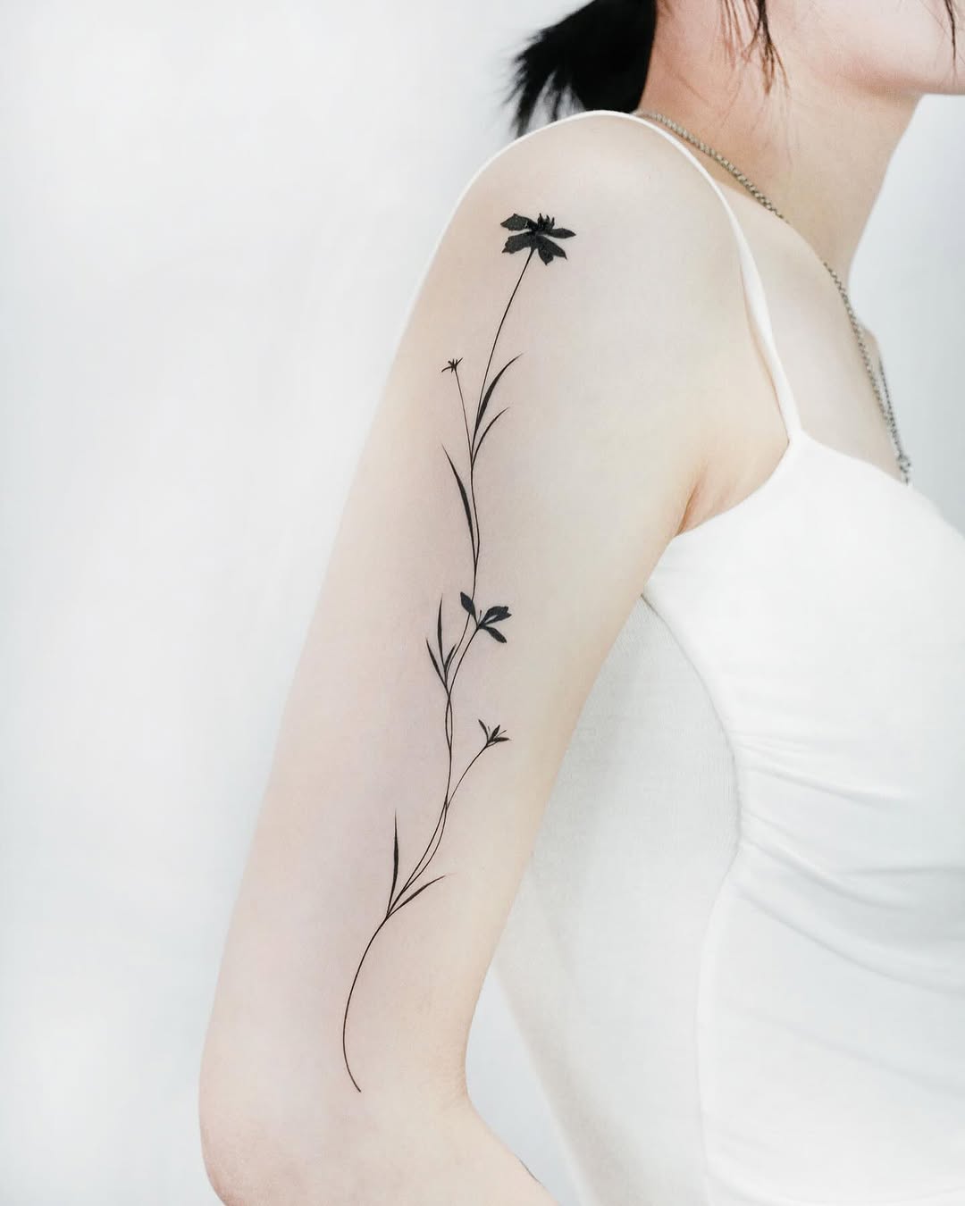 Single flower stem blackwork tattoo on the upper arm by 초현실과 현실 그 사이를 그리다.
