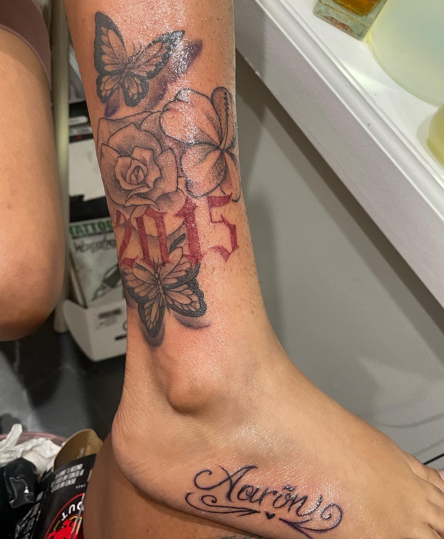 Flowers and butterflies black and grey tattoo on the foot by Aja Marie